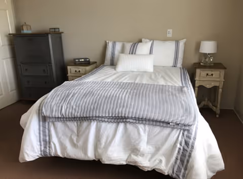 Neatly made bedroom with a bed, two nightstands, dresser, and a lamp.