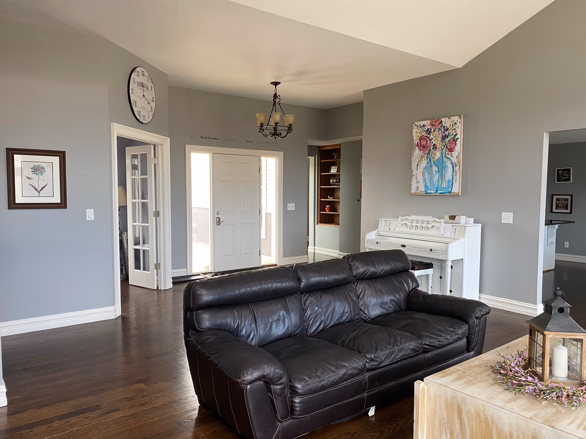 Gray-walled living room with a black leather sofa, white piano, and hardwood floors.