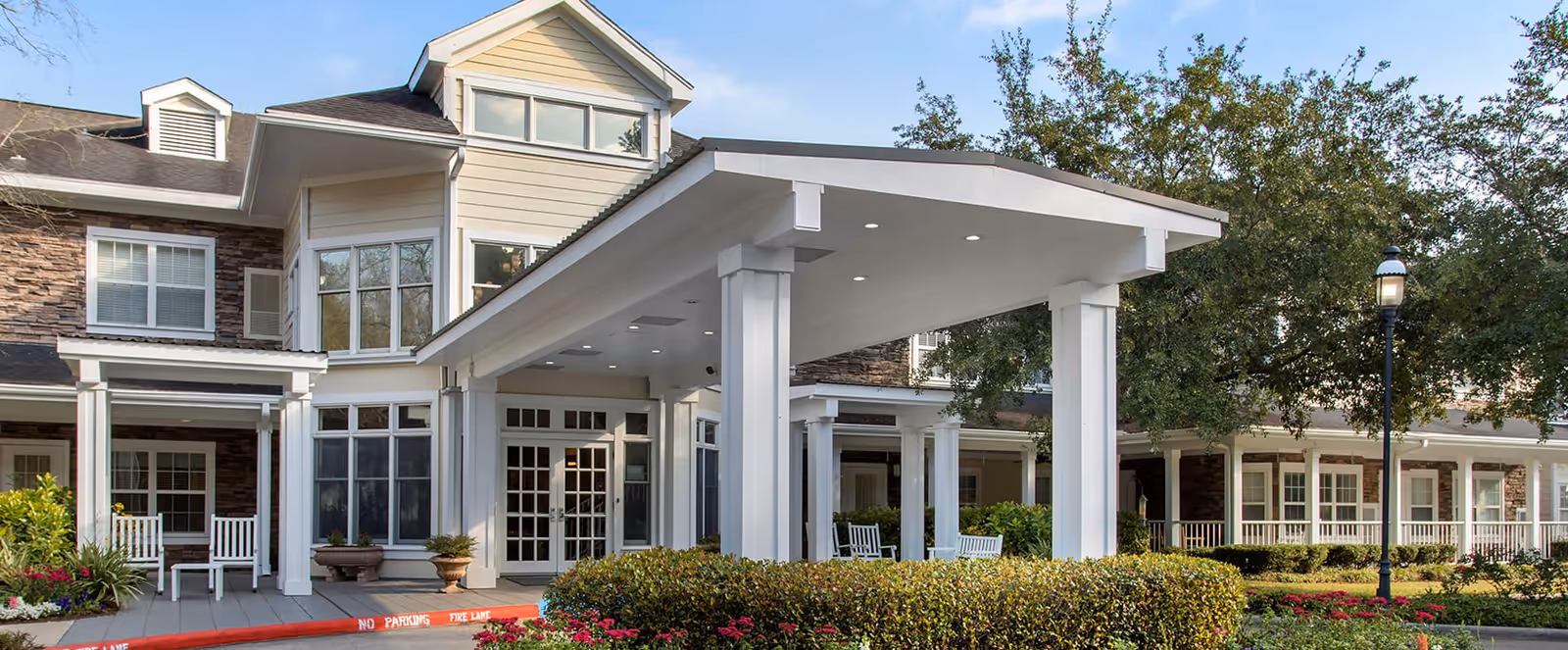 Exterior view of Brookdale Champions entrance with white columns, a covered drive, and seating.