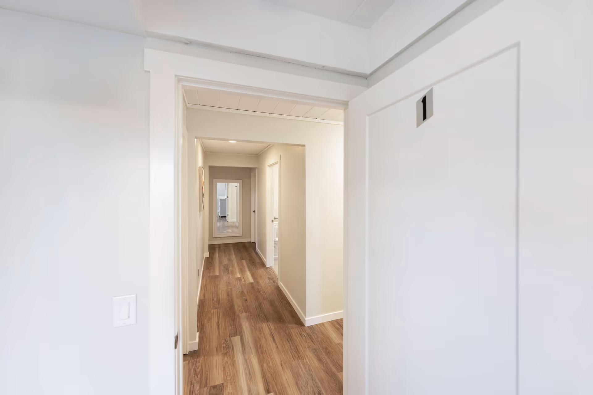 White-walled hallway with wood-look flooring and closed doors.