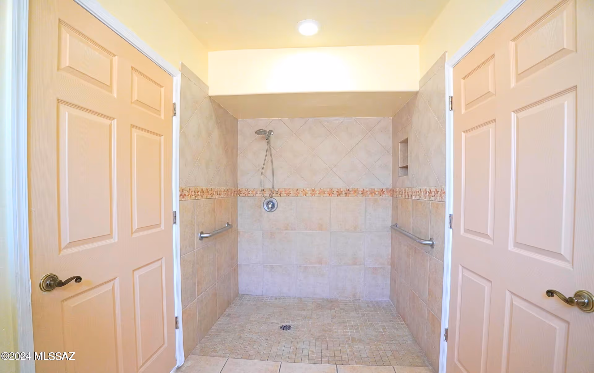 Two beige doors frame a tiled walk-in shower with grab bars.