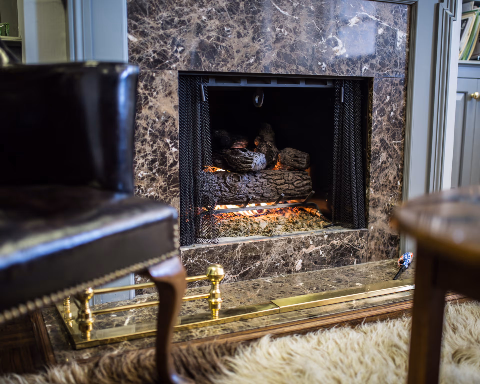 Stone-framed fireplace with glowing embers, marble surround, and nearby chairs.