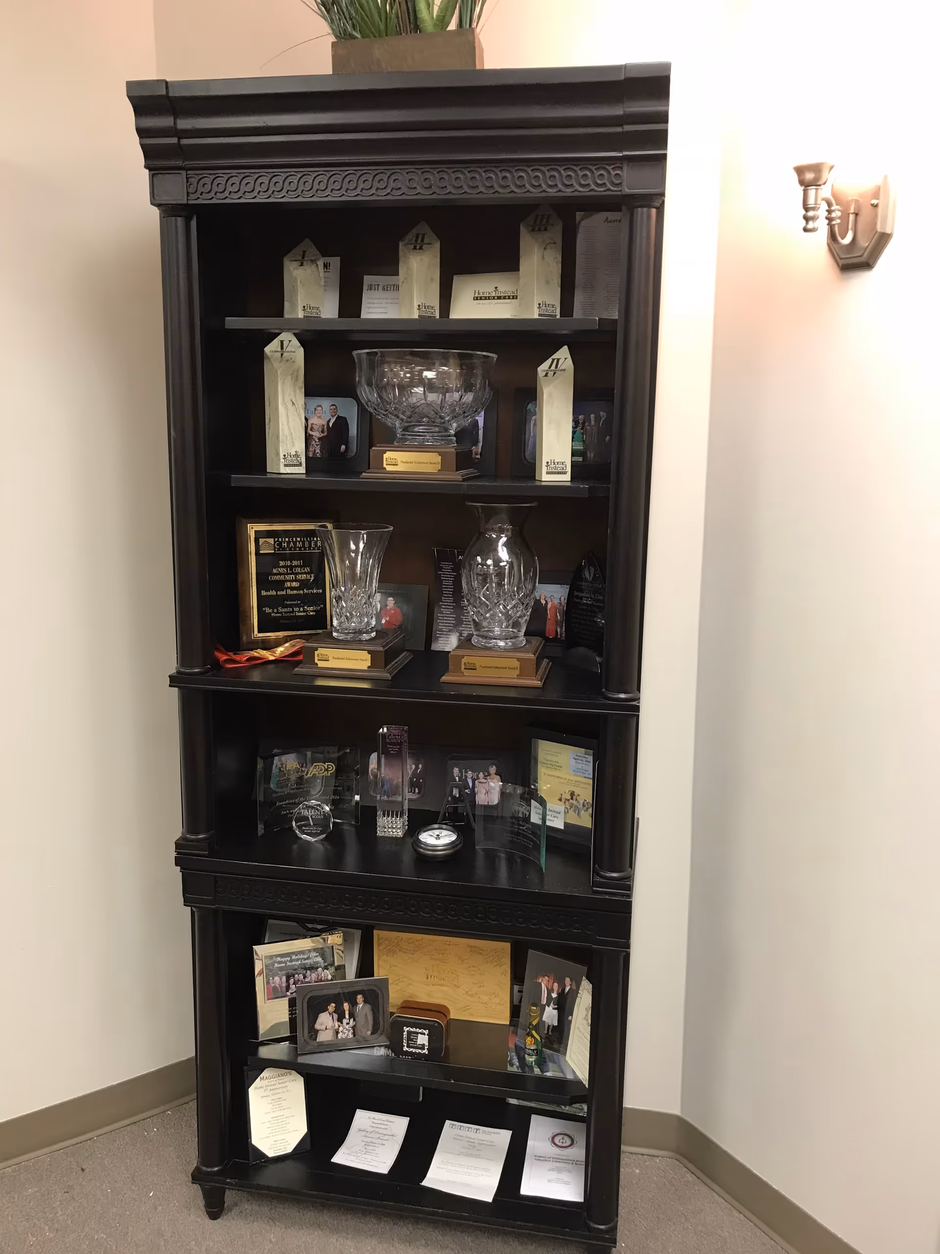 Dark wooden display cabinet housing glass trophies, plaques, photos, and memorabilia in a hallway.