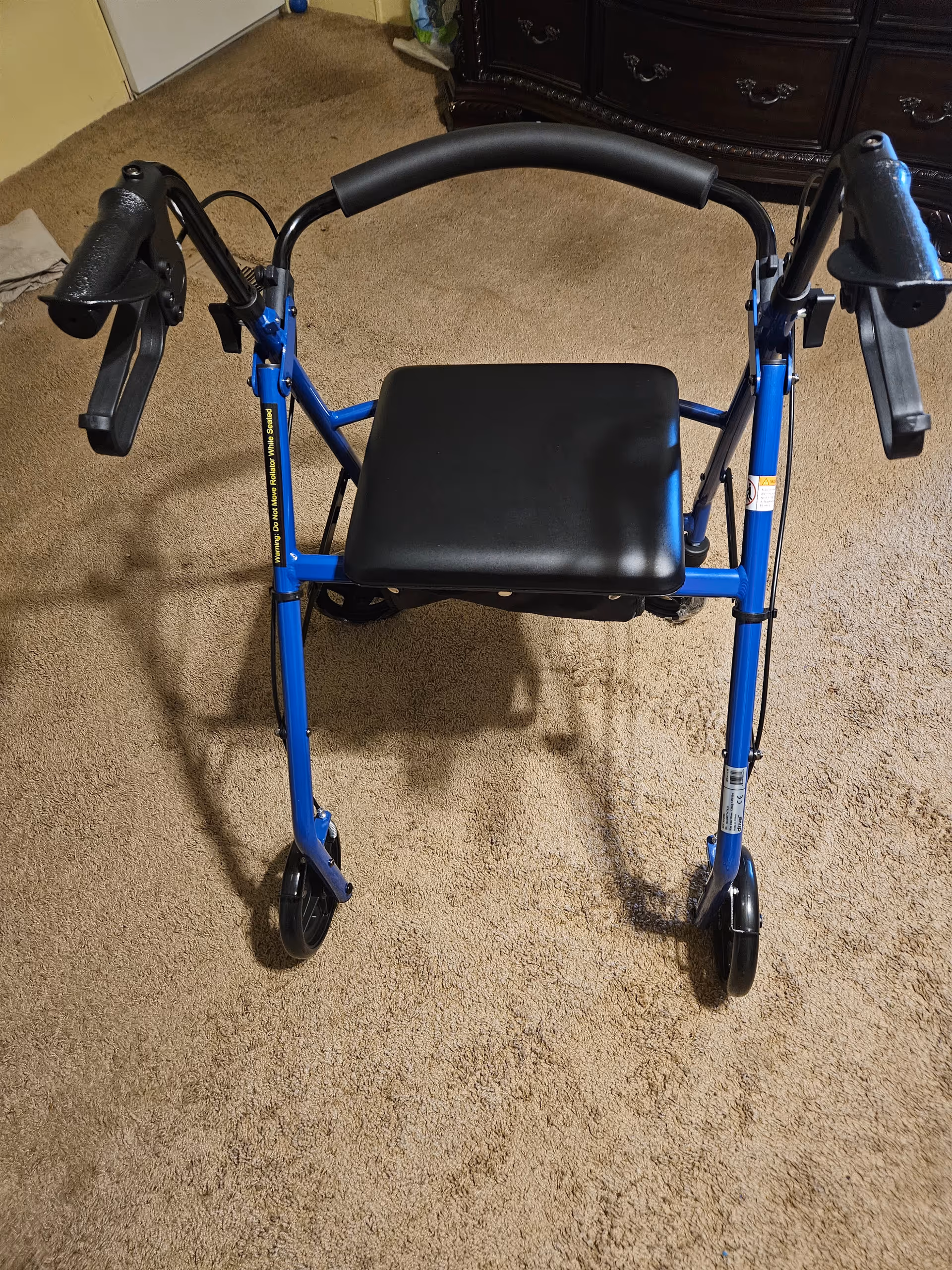 Blue walker with a black seat stands in a carpeted indoor room.