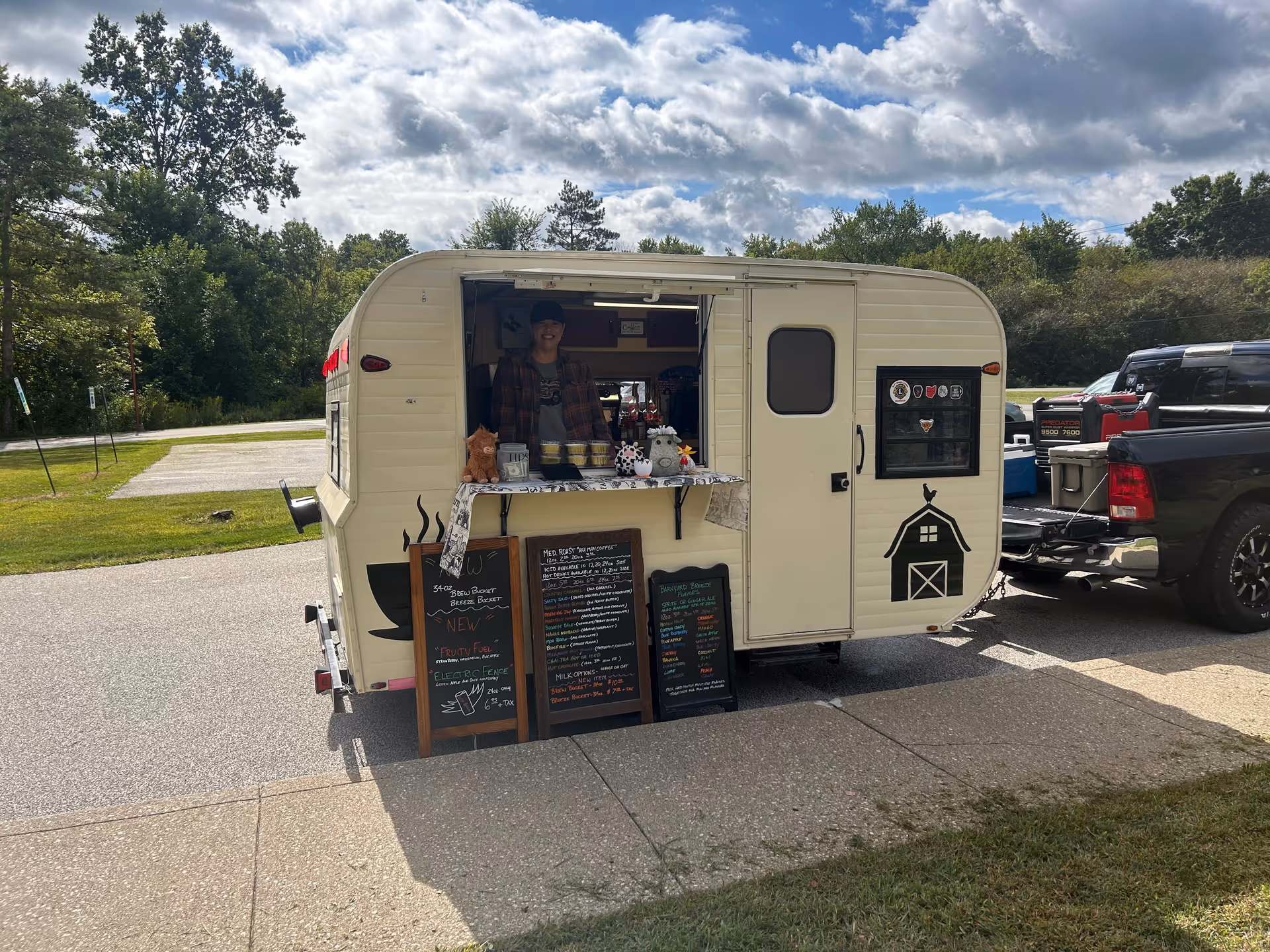 A person in a plaid shirt operates a mobile outdoor concession trailer.