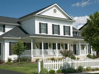 Exterior view of a white senior living home with a wraparound porch and hanging plants.
