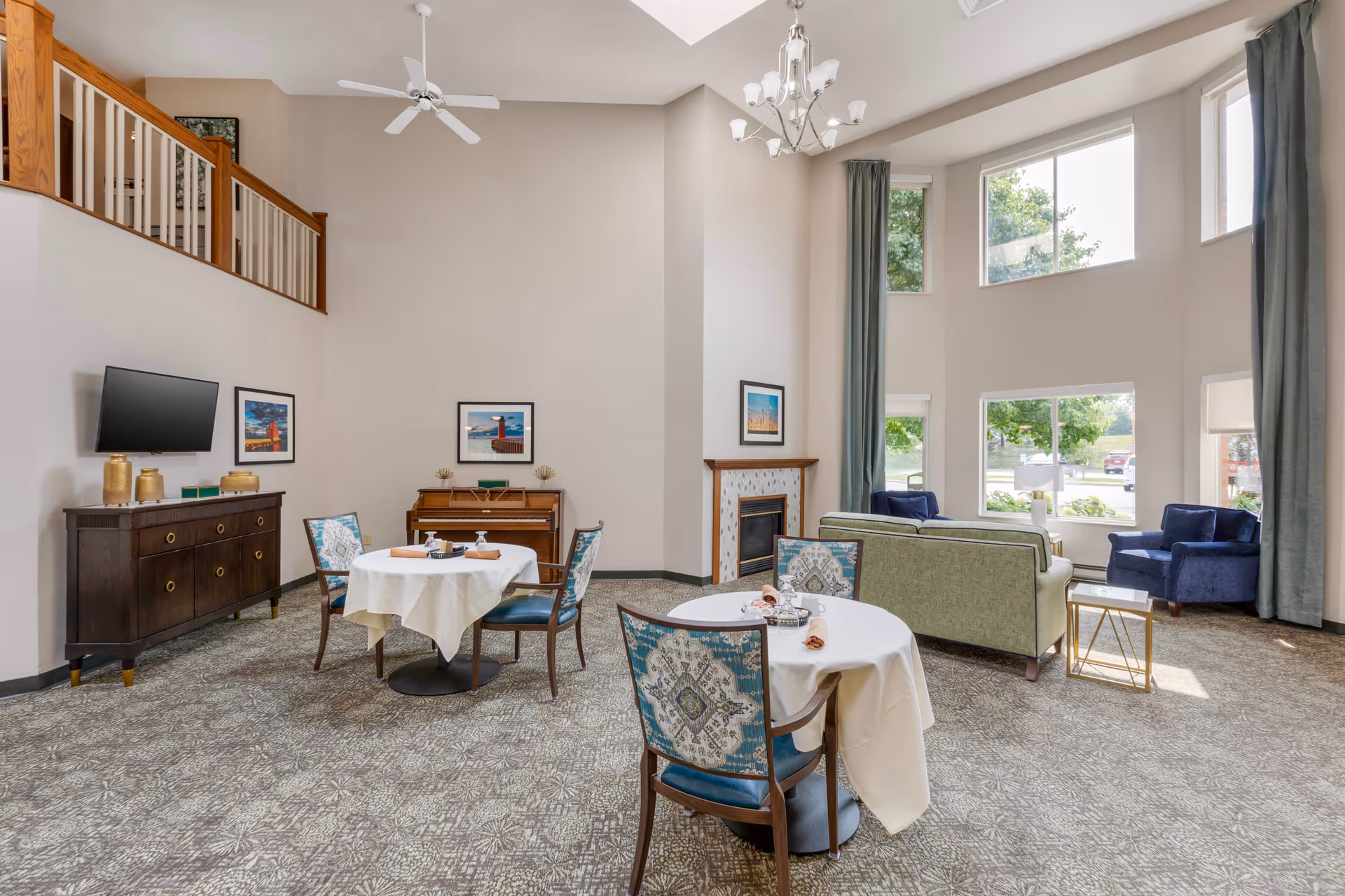 Spacious senior living lounge with seating, tables, a fireplace, and large windows.
