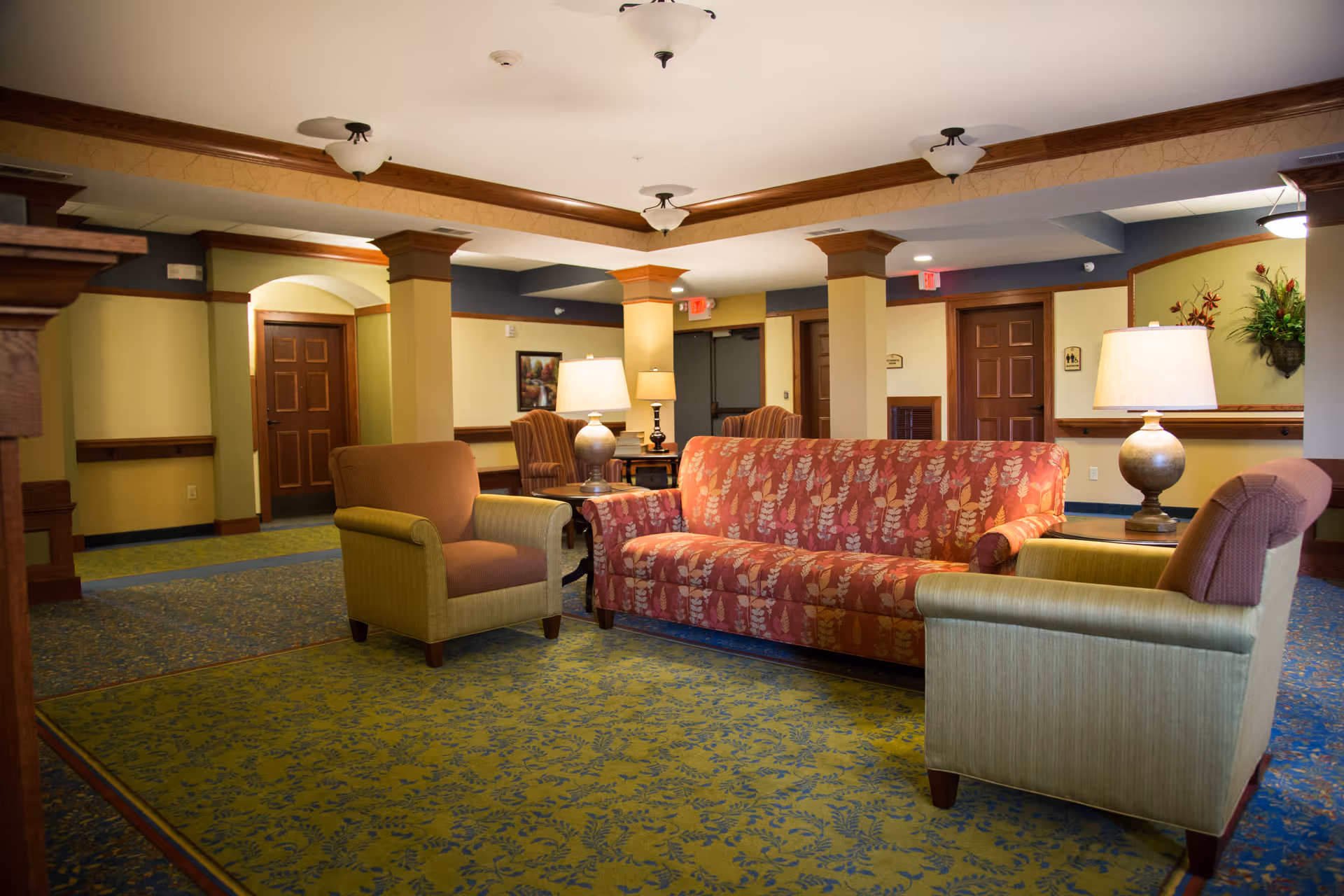 Senior living lobby lounge with patterned sofa, armchairs, lamps, and carpet.