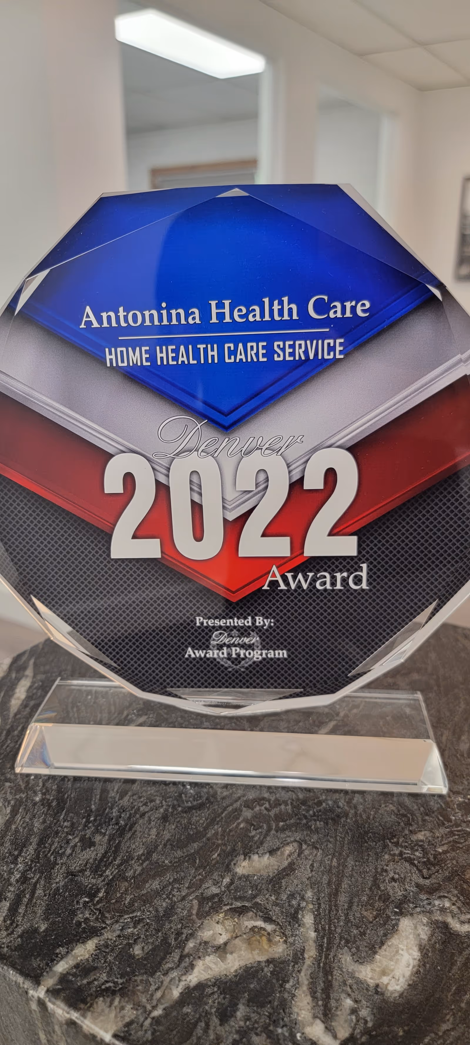 A trophy award sits on a dark marble countertop featuring Antonina Health Care branding.