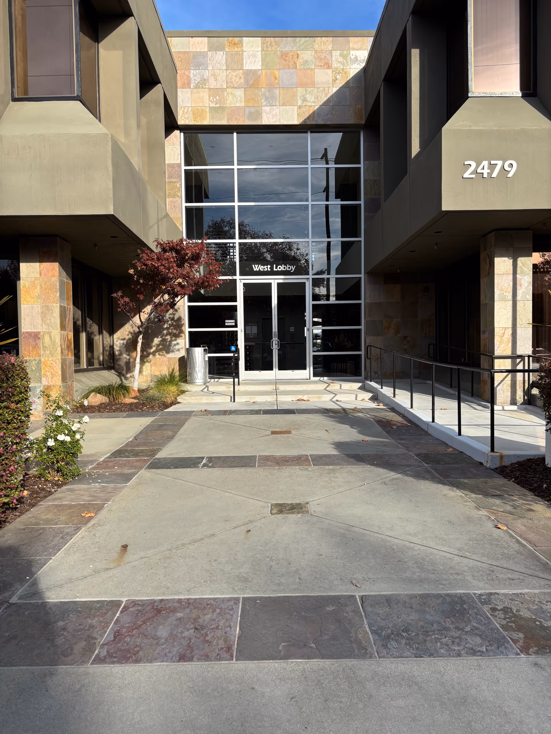 Modern building entrance with glass doors labeled West Lobby and stone facade.