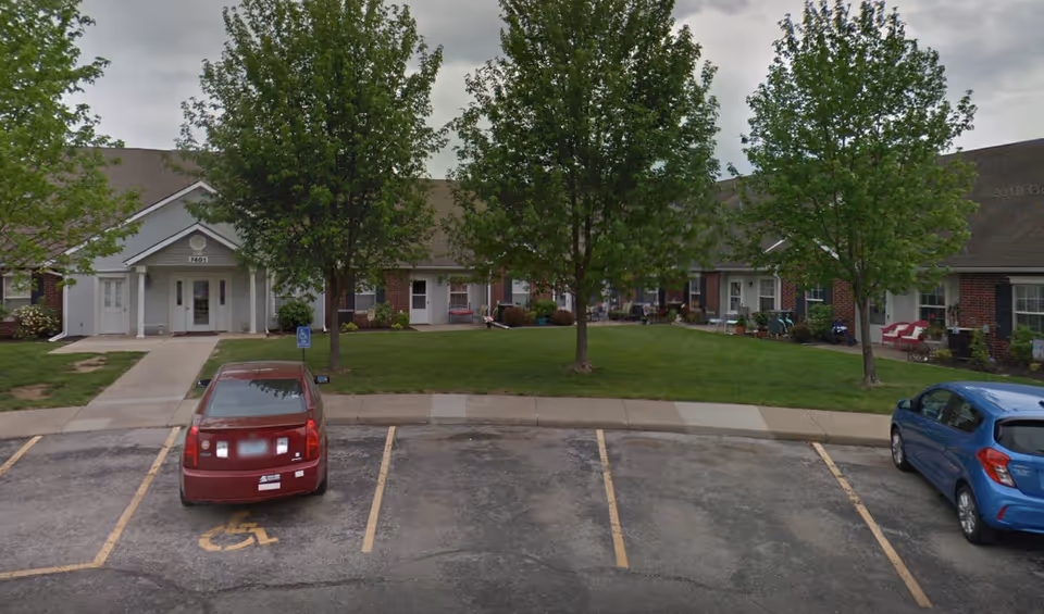 Exterior view of Elliott Place Senior Living with a green lawn, trees, and parked cars.