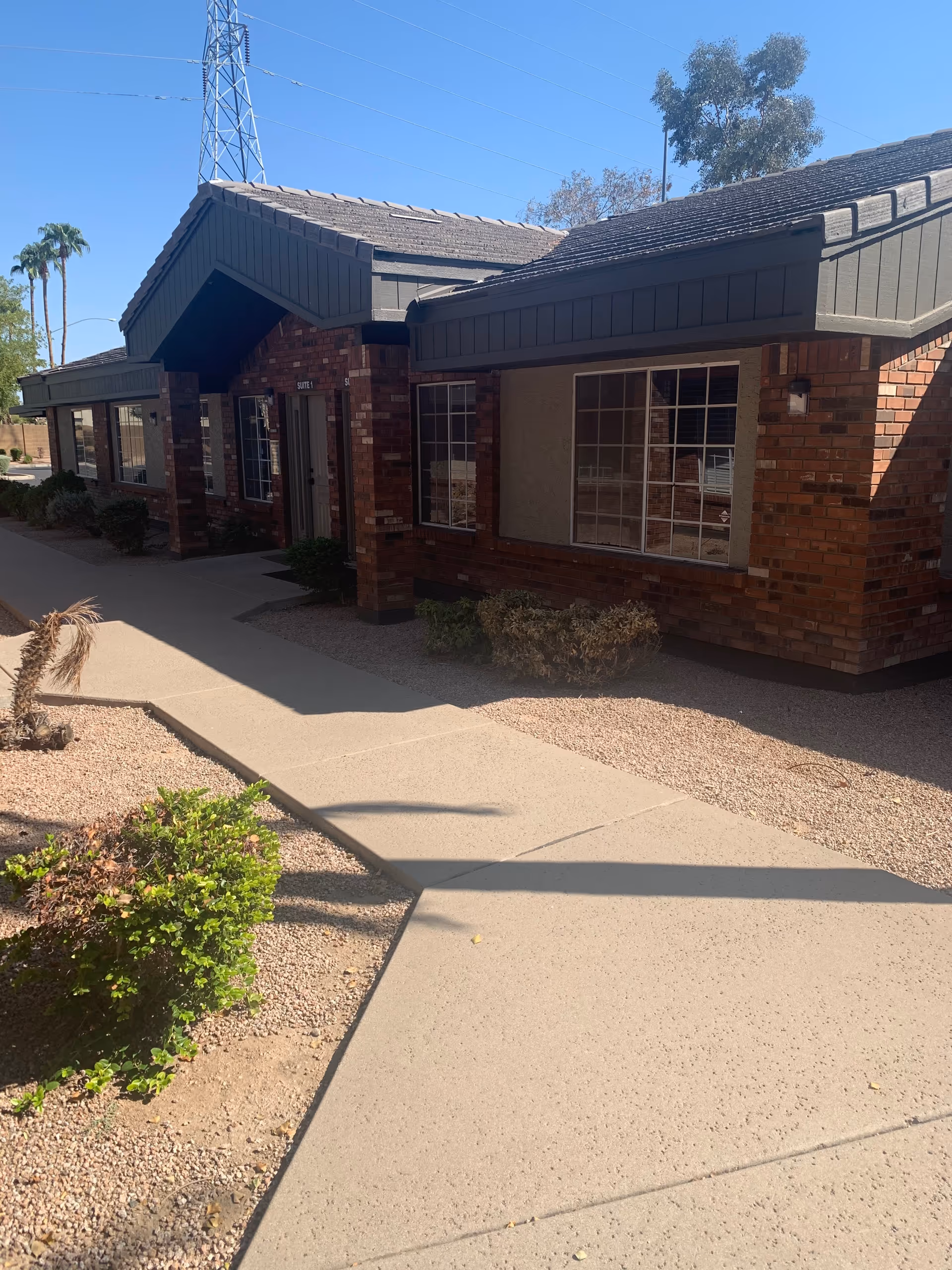 Exterior view of a brick senior care facility with a sidewalk and desert landscaping.