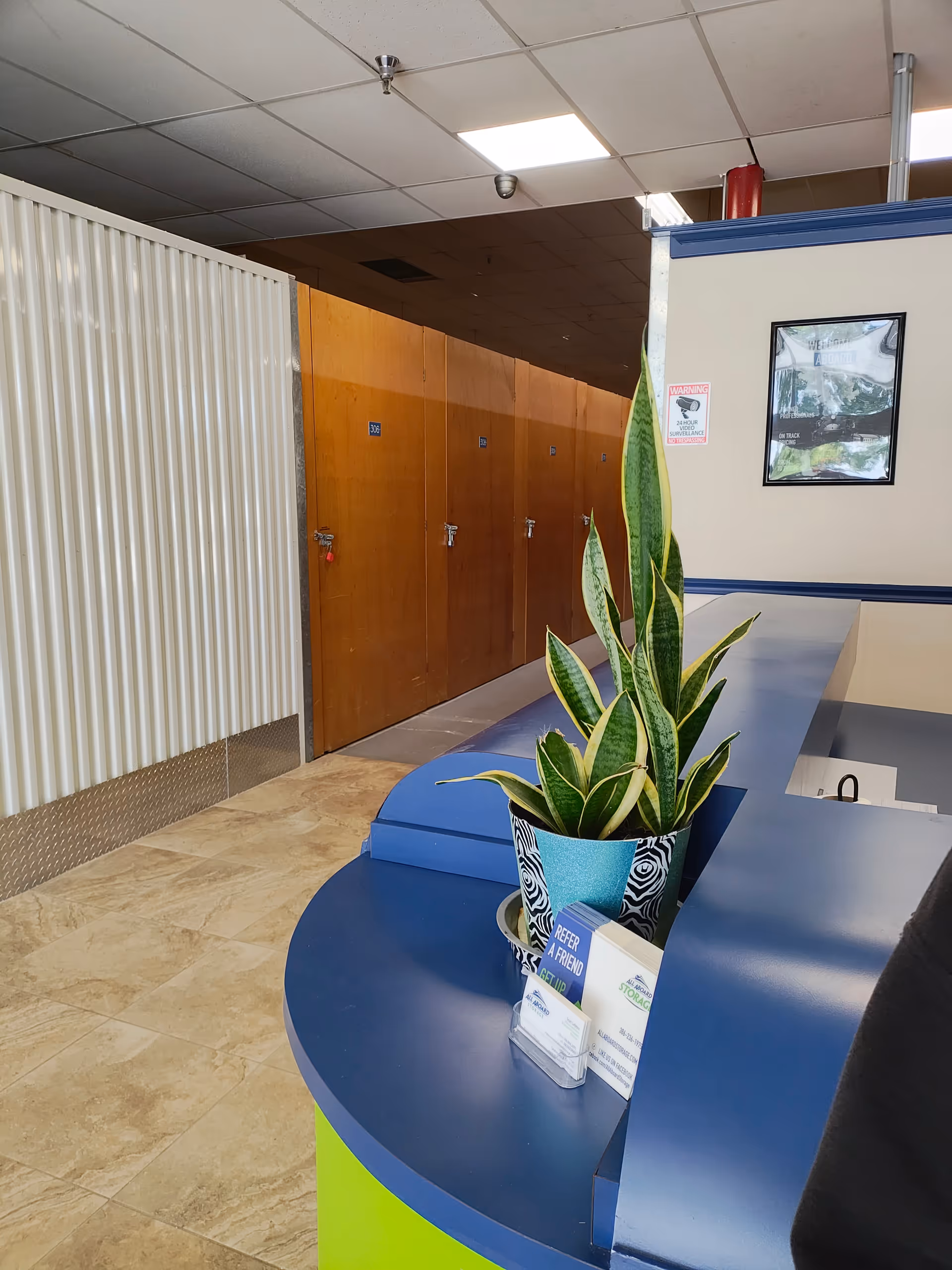 Reception desk with blue surface, plant, and wooden doors along a hallway interior.