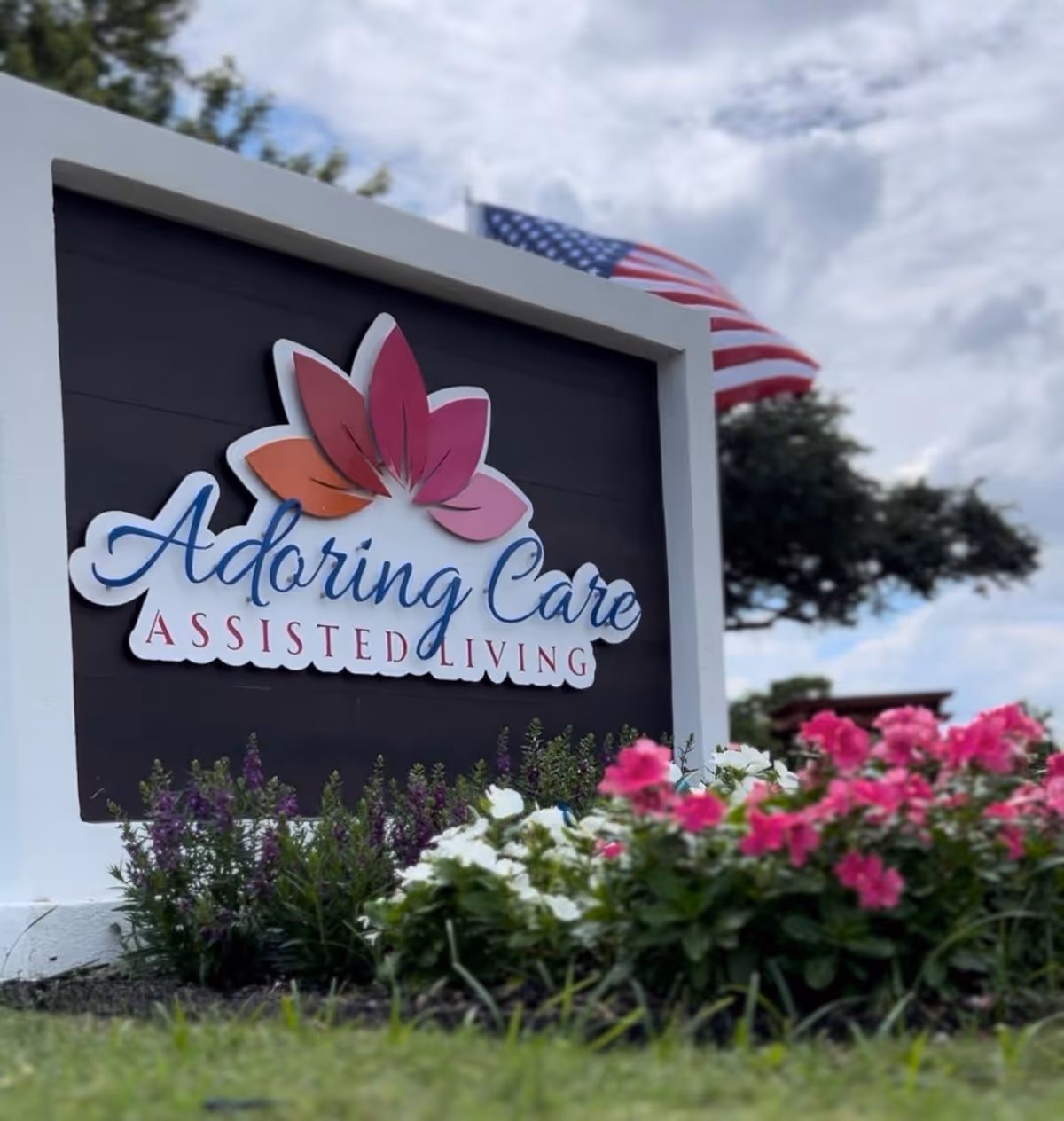 Sign reads Adoring Care Assisted Living with colorful flowers in the foreground.