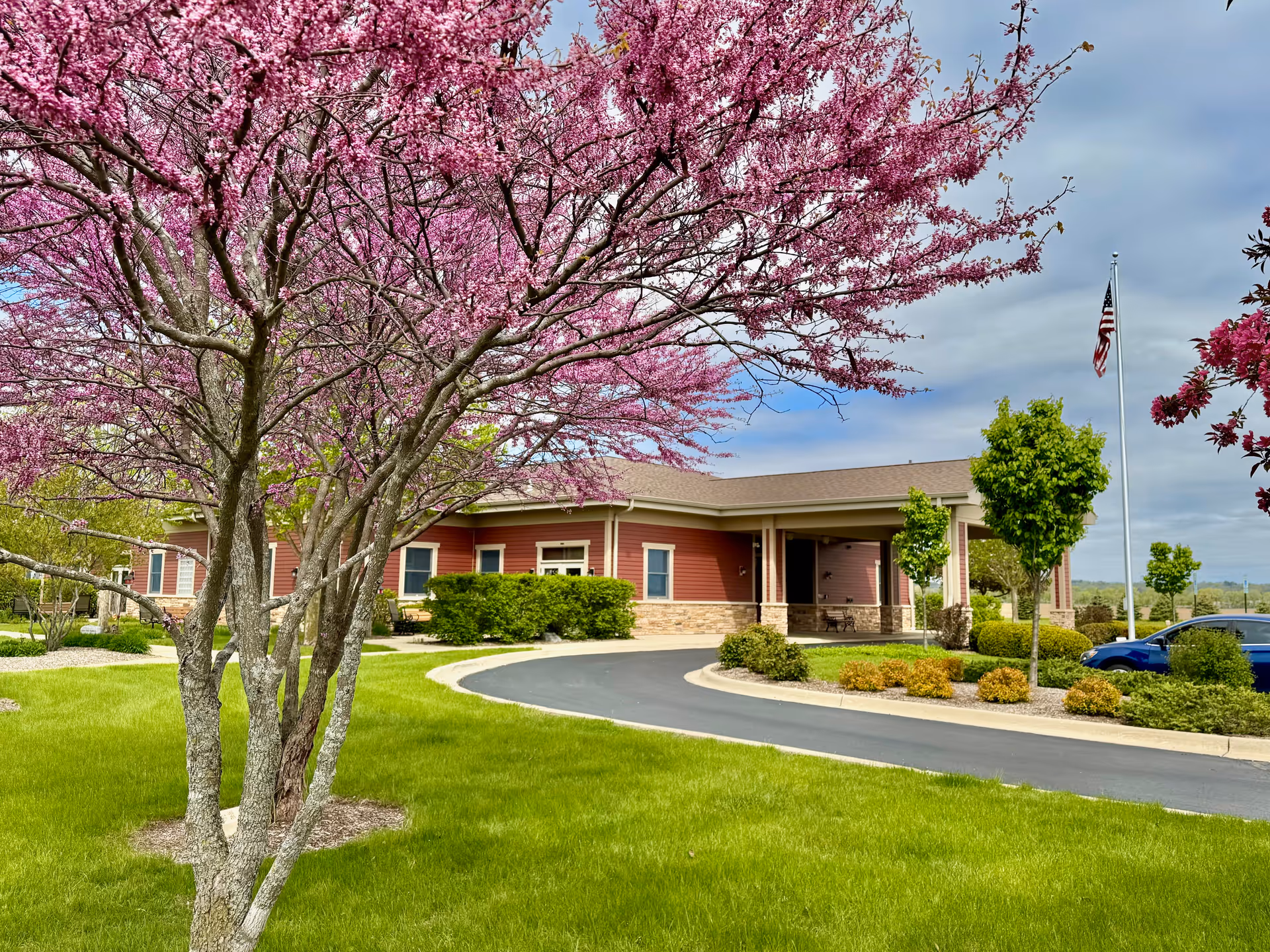 Exterior view of Serenity Hospice and Home: red brick building with curved driveway and pink blossoms.
