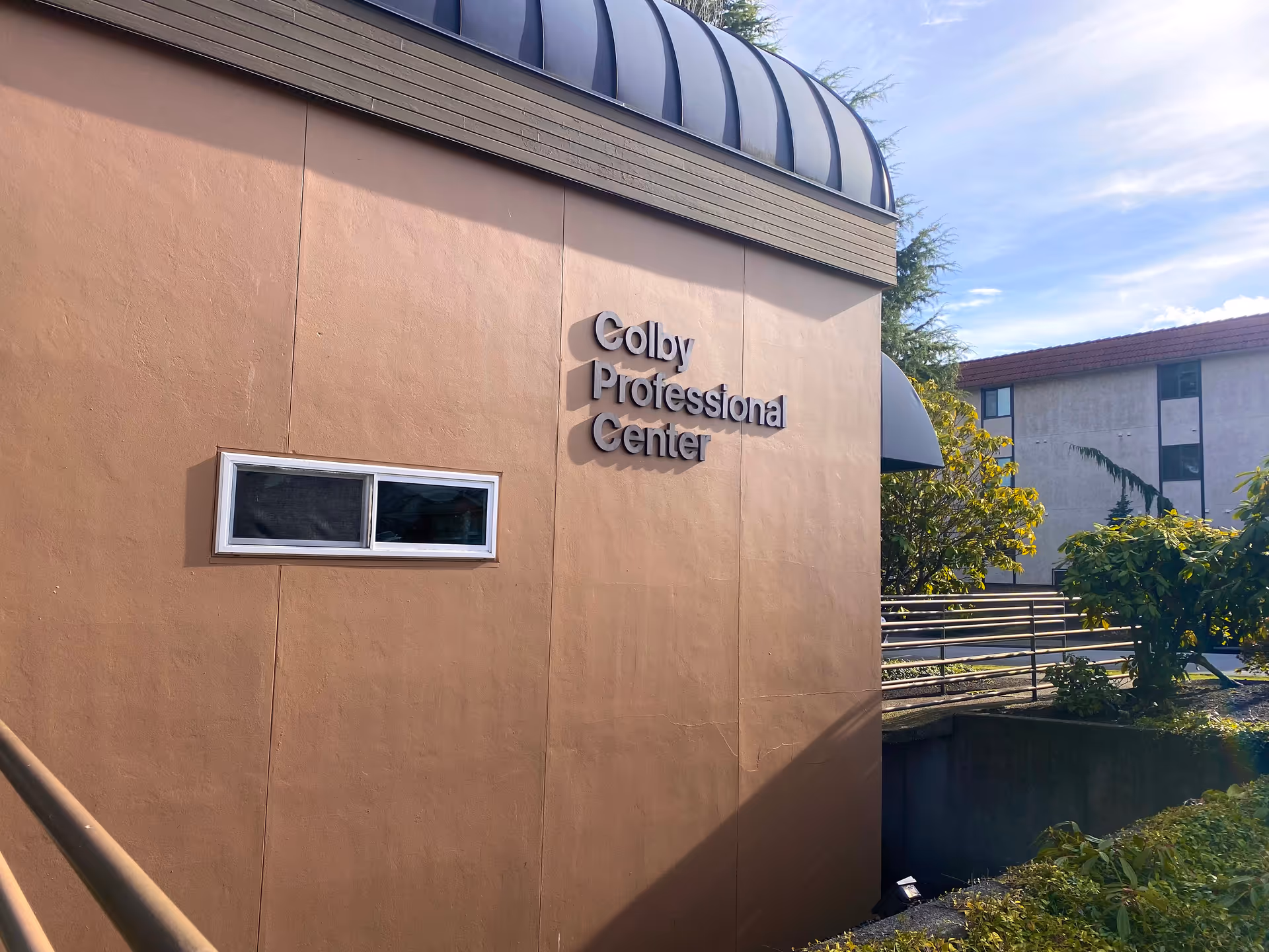 Exterior view of a tan building with Colby Professional Center sign and greenery
