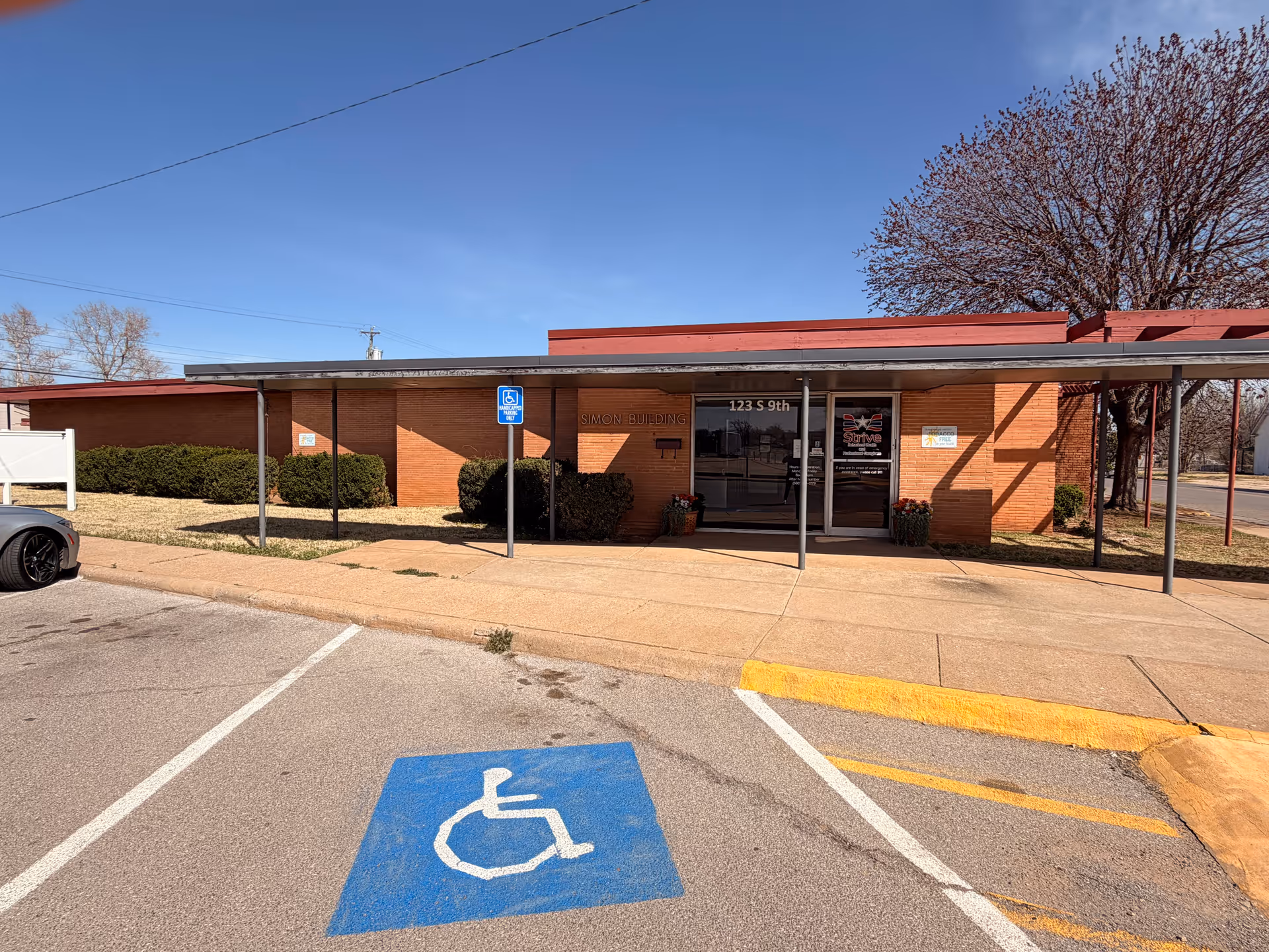 Brick facility with glass entrance, wheelchair parking sign, and accessible parking in foreground.