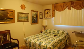 Cozy bedroom with a quilted bed, wall art, lamp, and window blinds.