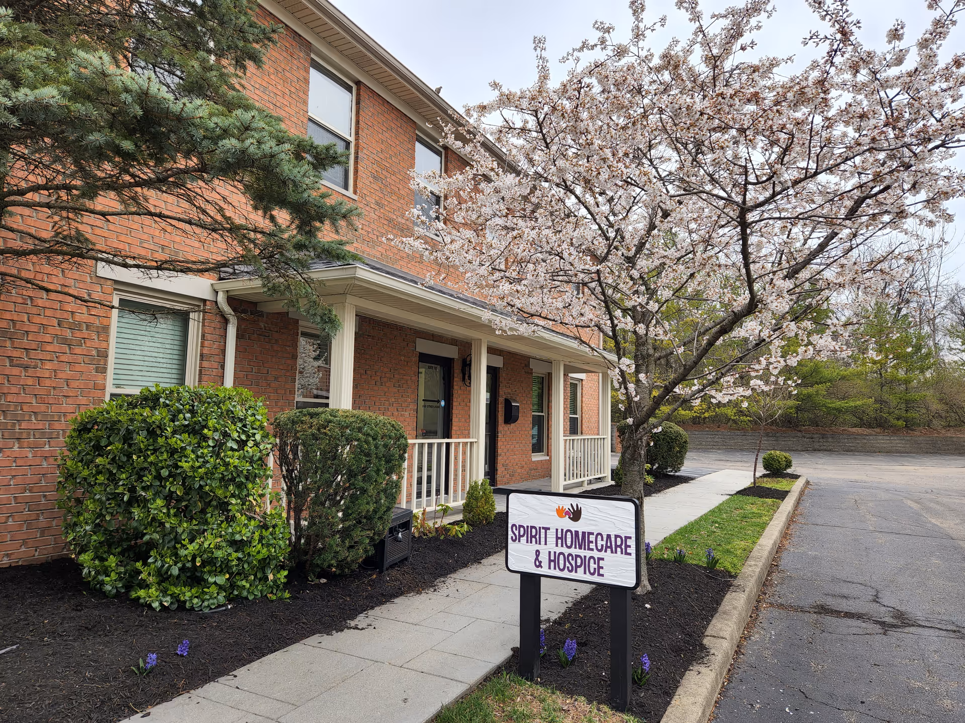 Brick senior care building with a flowering tree, sidewalk, and Spirit Homecare & Hospice sign.