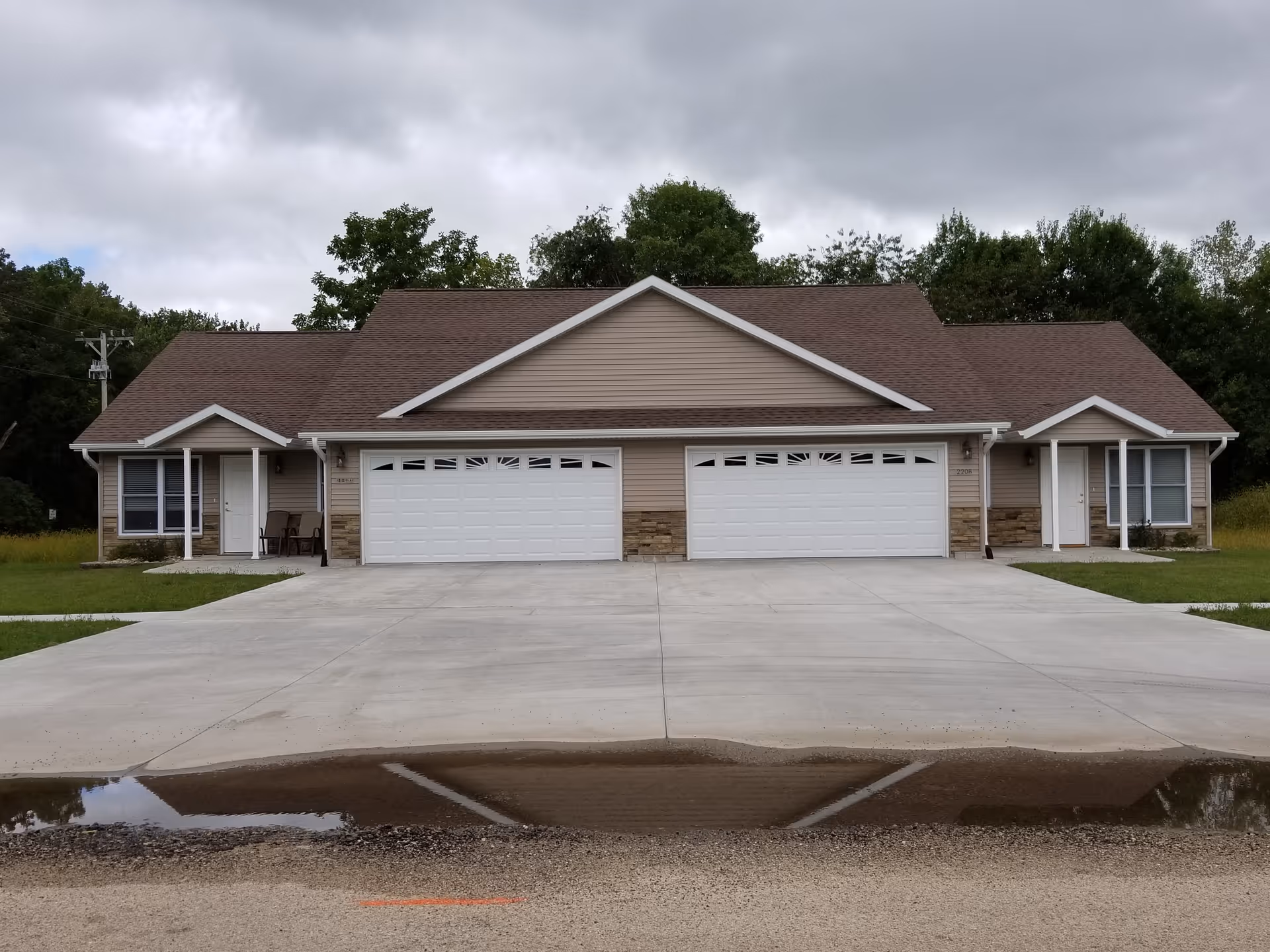 Front exterior of a beige, suburban-style building with a three-garage facade and green lawn.