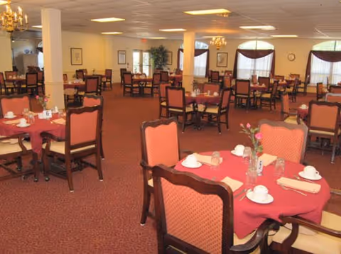 Spacious dining room with red tablecloths, place settings, and chairs.