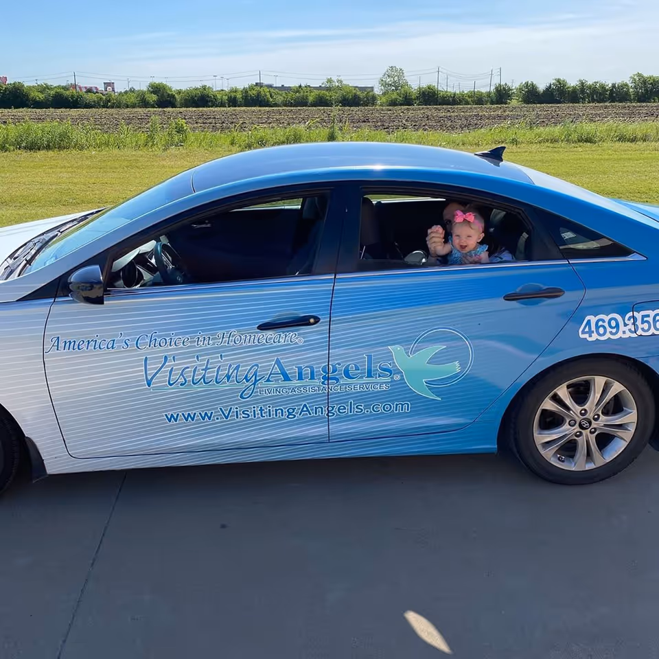 Blue Visiting Angels car shows branding; a child sits in the back seat with rural backdrop.