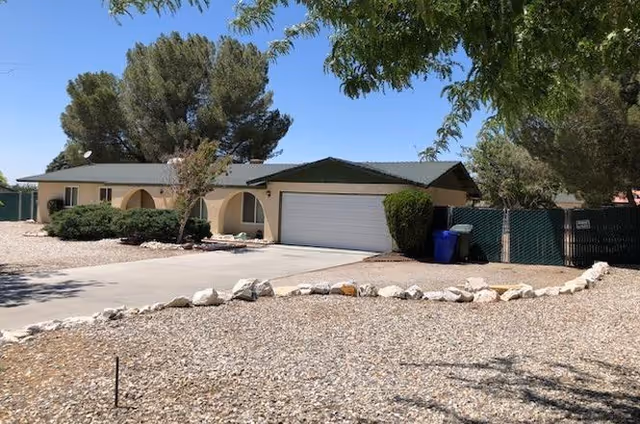 One-story beige building with arched entryways, a two-car garage, and desert landscaping.