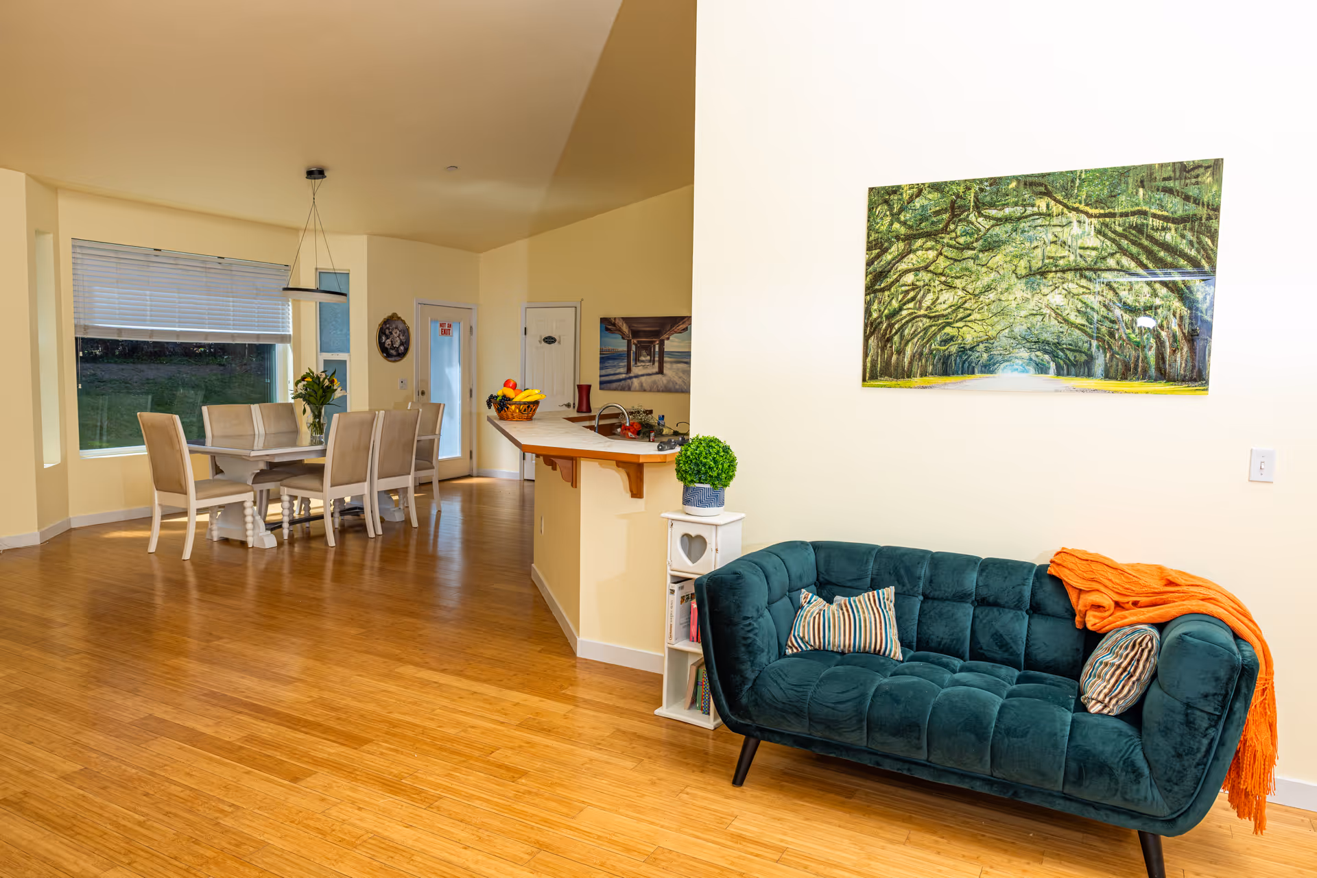 Open living area with teal sofa, dining table, kitchen counter, and wall art.