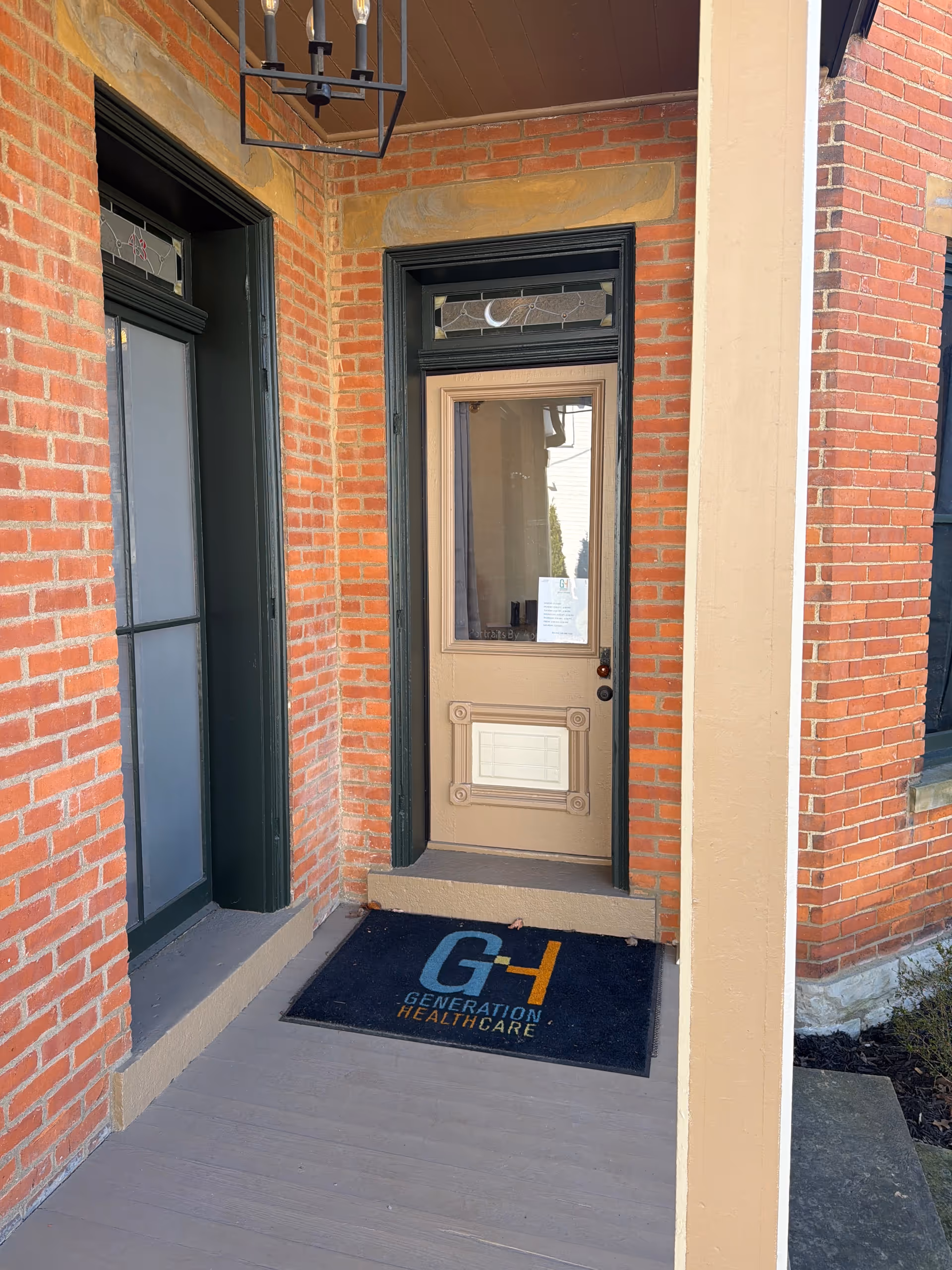 Brick building entrance with a beige door, black trim, and a Generation Healthcare mat.