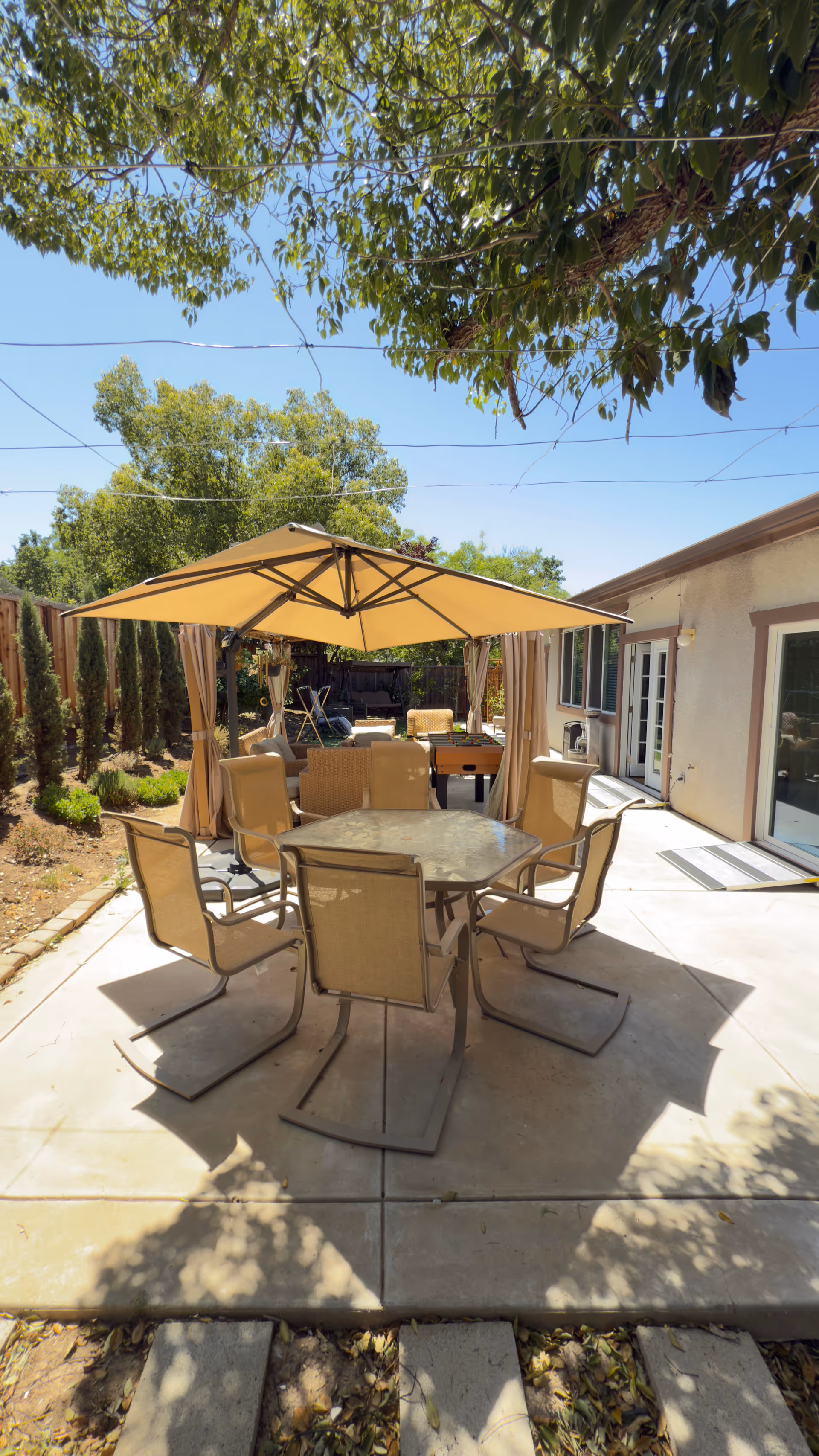 Outdoor patio setting with table, shade umbrella, and seating along a house.