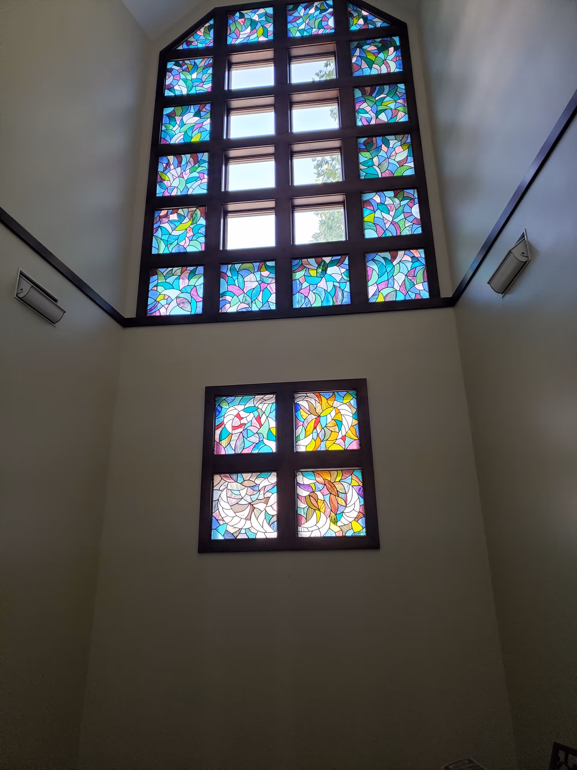 Tall interior atrium with colorful stained glass windows on light walls.