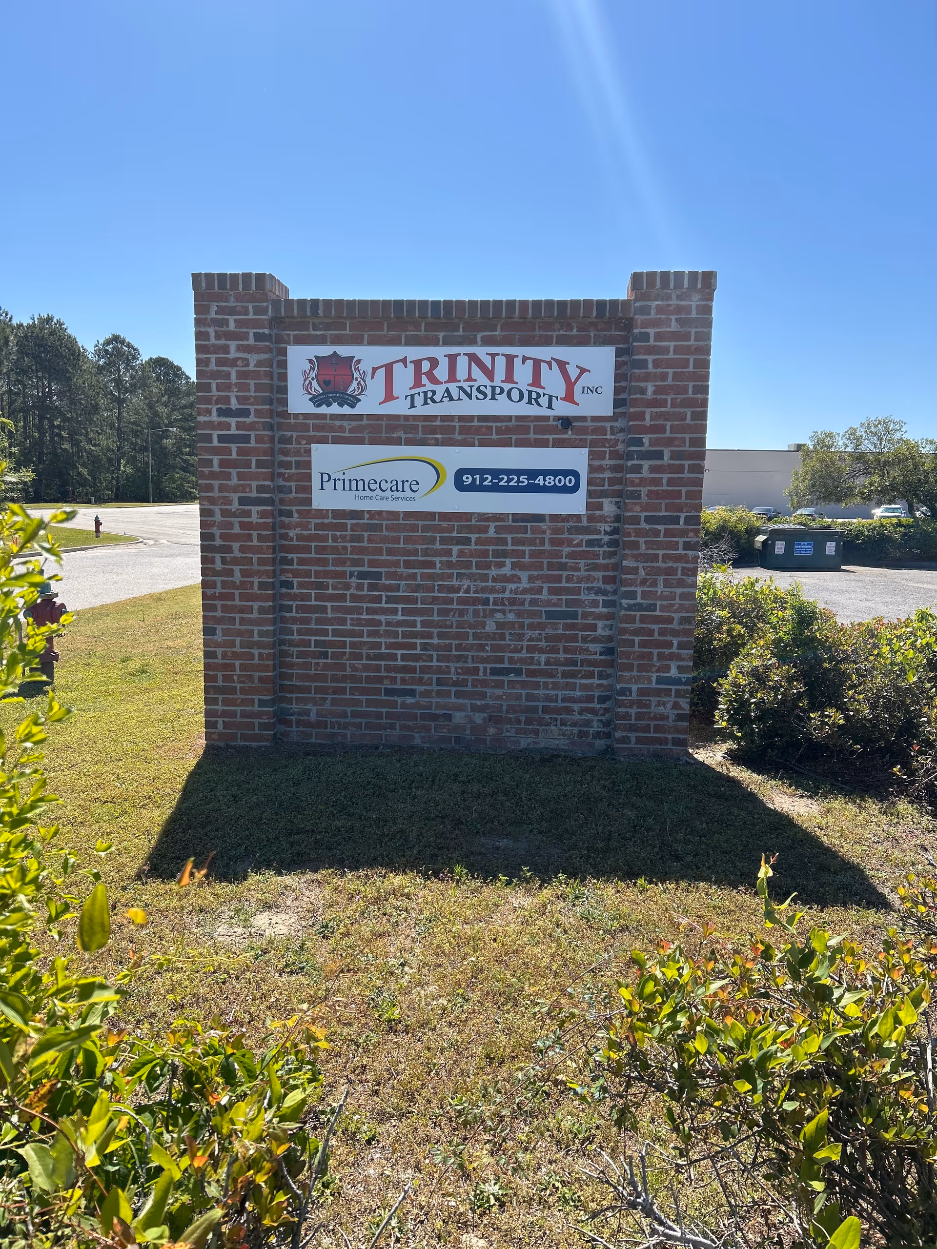 Brick sign structure with Primecare Home Care Services and Trinity Transport signs outdoors.