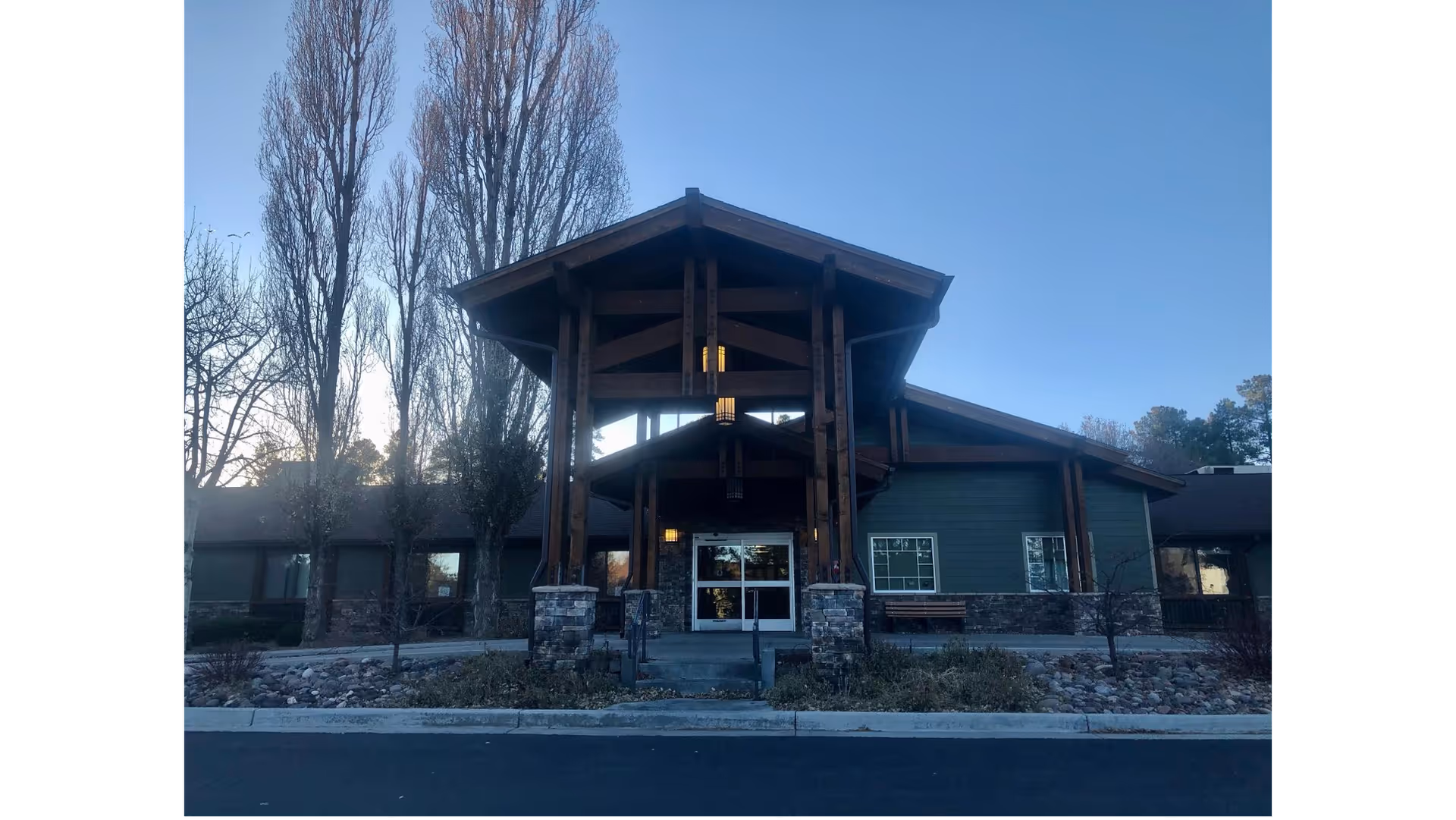 Front exterior view of Haven Health Flagstaff building with a wooden peaked entrance supported by stone pillars, surrounded by leafless trees and landscaping under a clear sky.