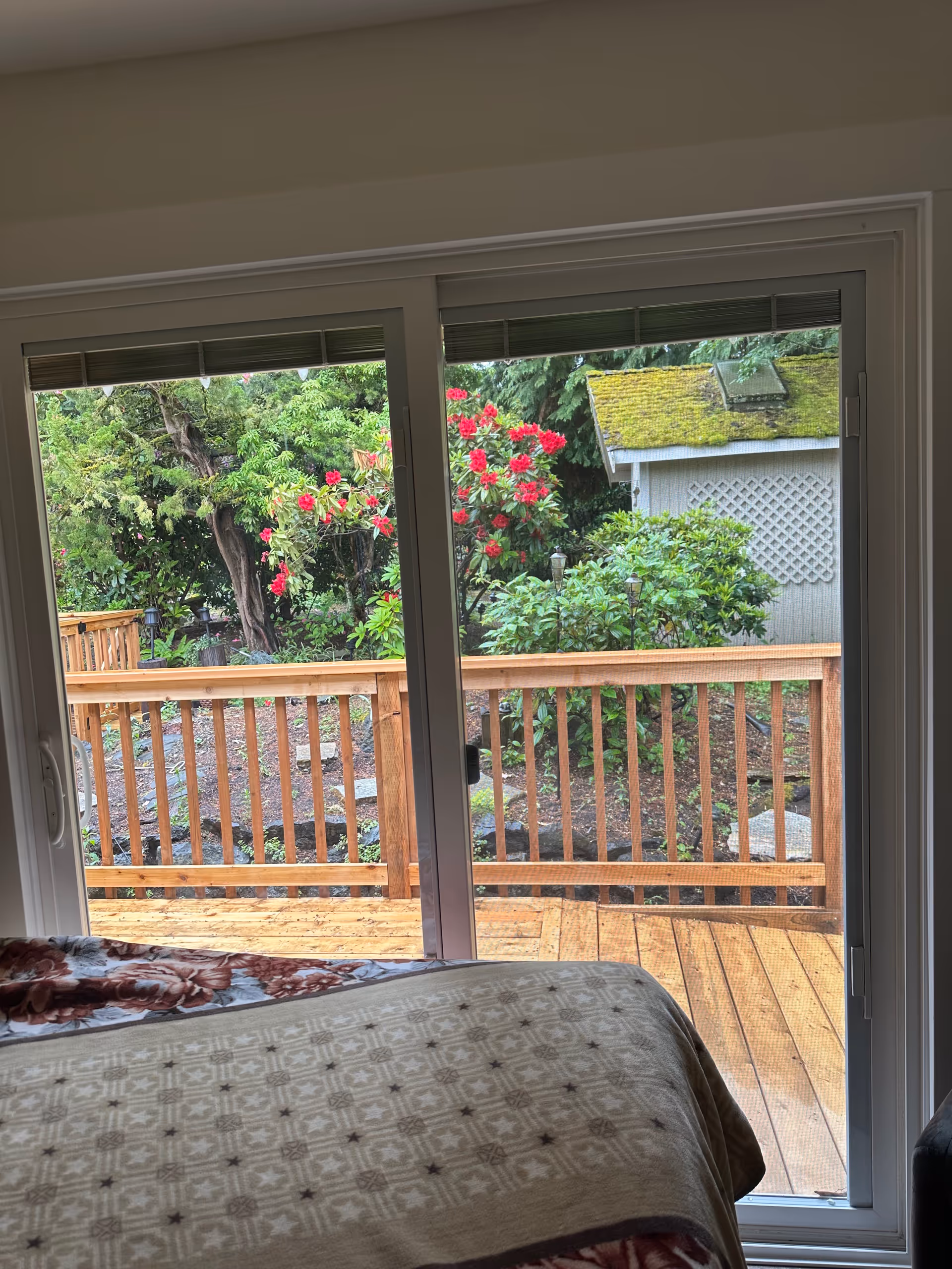 Bedroom with sliding glass doors to a wooden deck and lush garden beyond.