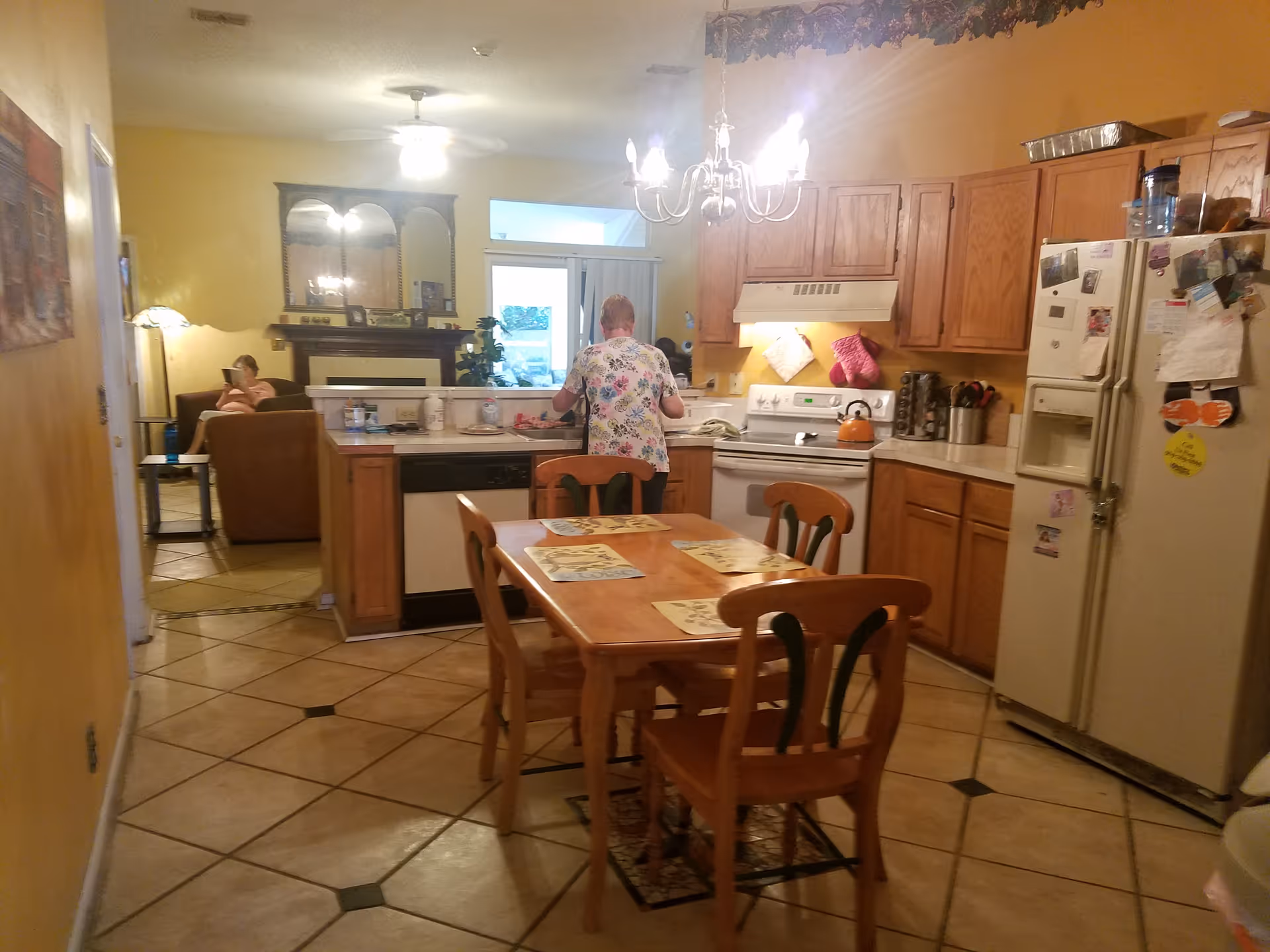 Cozy kitchen and dining area with wooden cabinets, table, and residents in background.