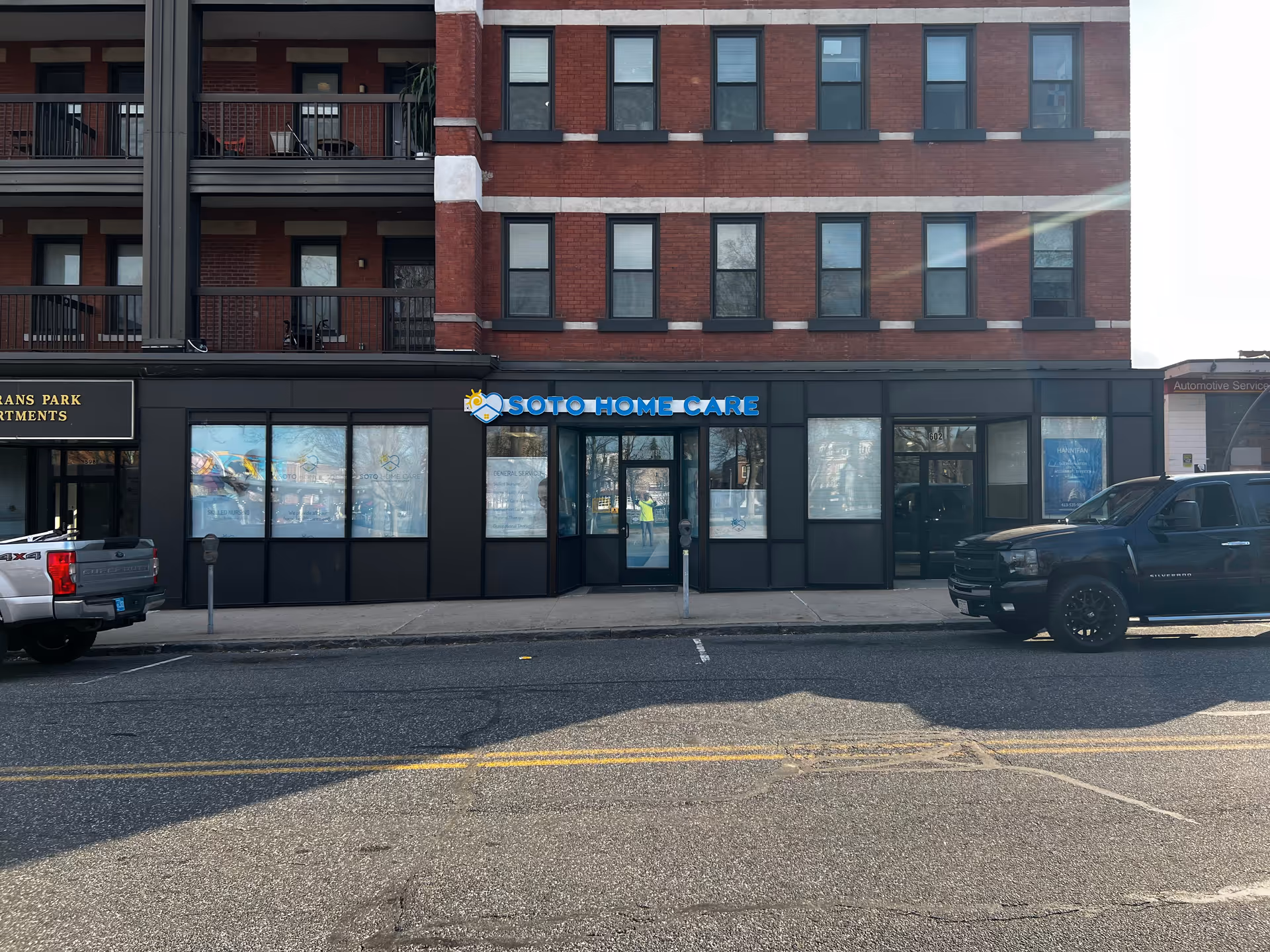 Brick three-story building with Soto Home Care storefront and parked vehicles on street.
