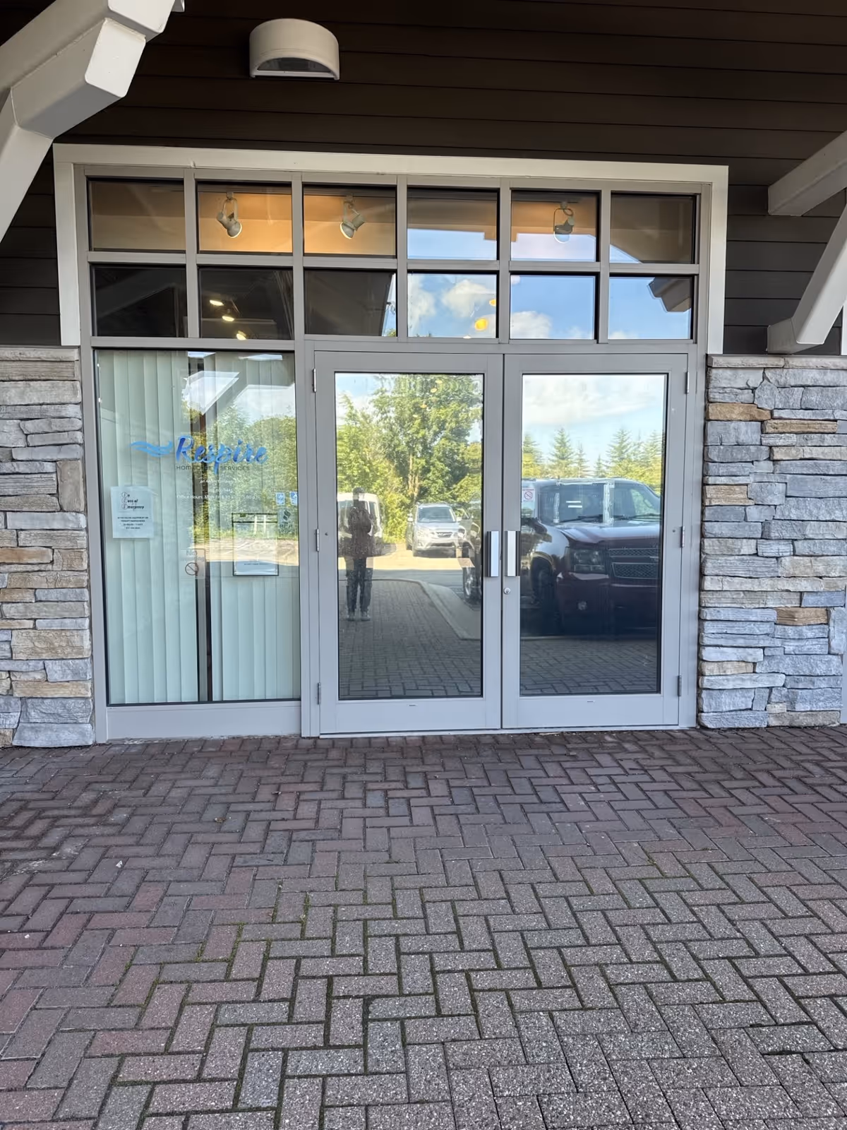 Double glass doors with stone facade entrance, brick walkway, and reflection of vehicles outside.