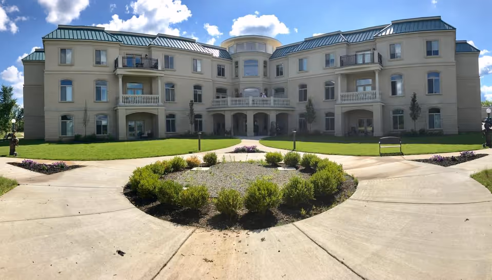 A large beige senior living building with a circular driveway and manicured landscaping.
