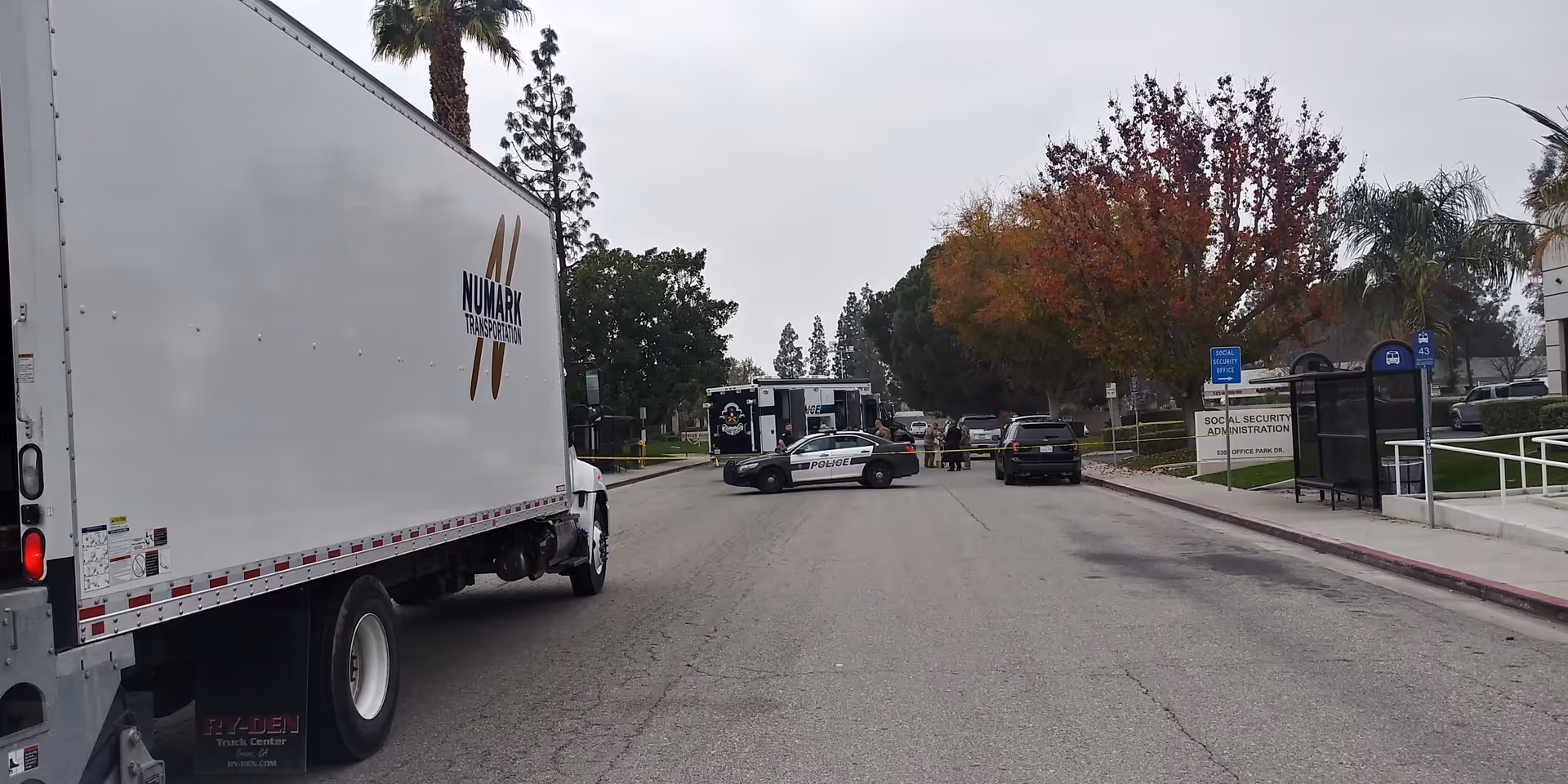 Exterior street scene with a large white truck, police cars, near a facility.