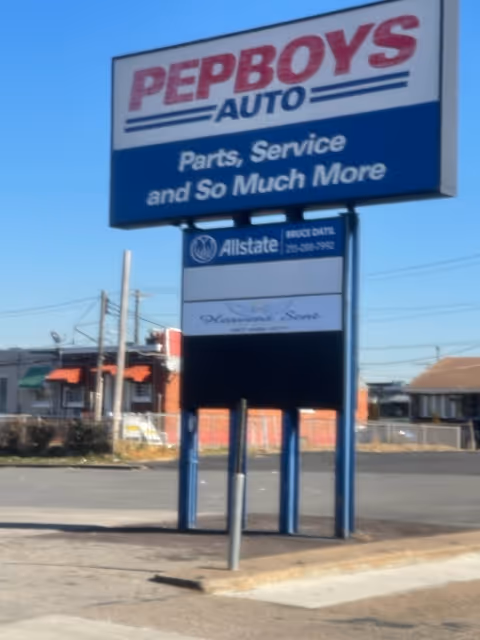 Large Pep Boys Auto sign over a street with storefronts and blue sky.