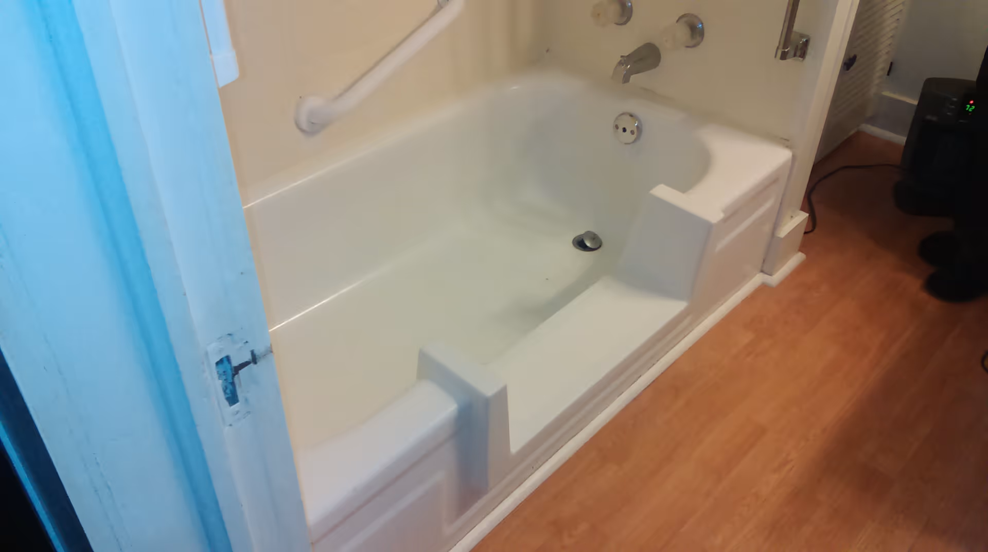 White bathtub with built-in seat and handrails in a small bathroom.