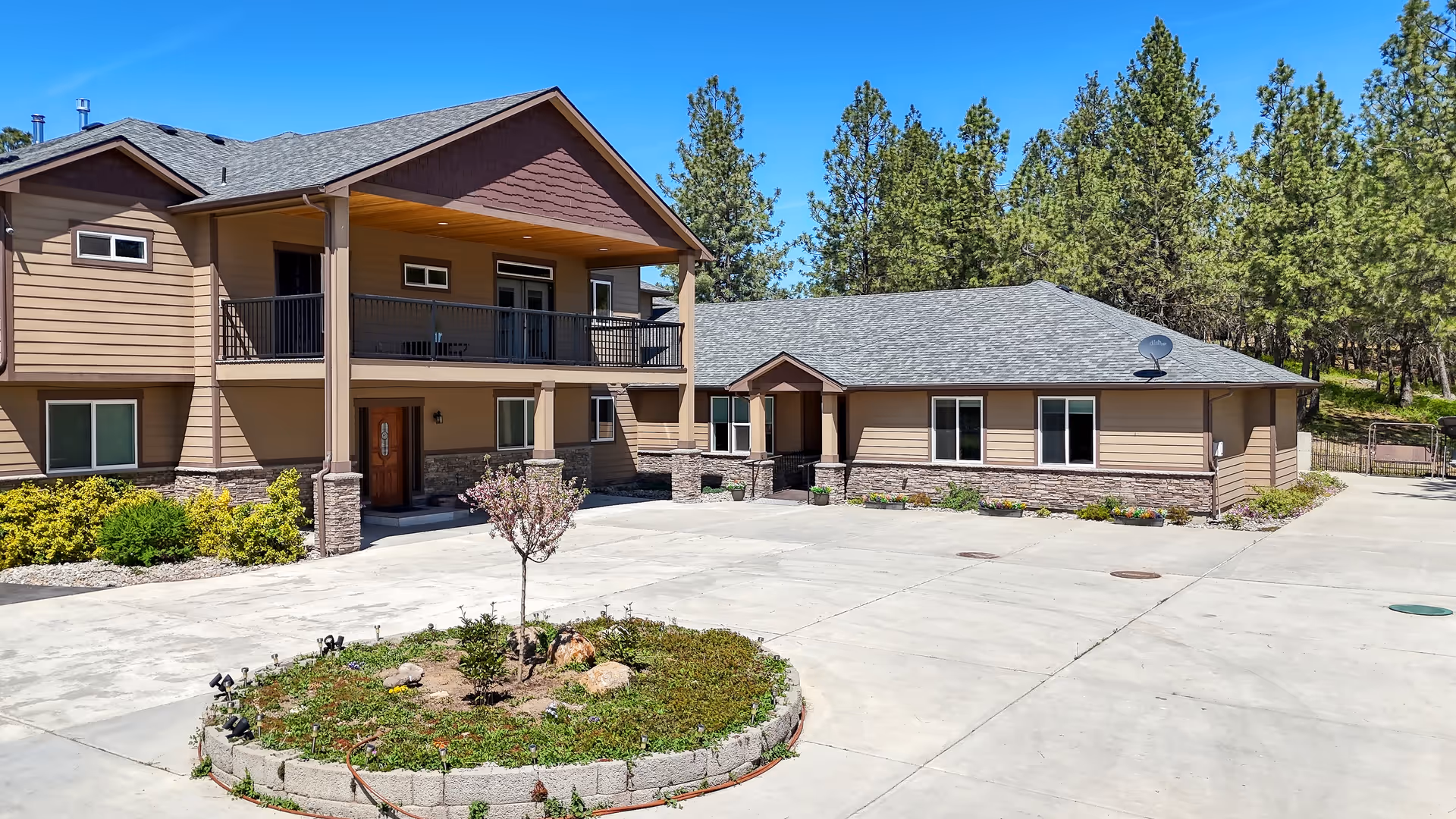 Two-story tan senior living facility exterior with balcony, paved lot, and circular landscaped island.