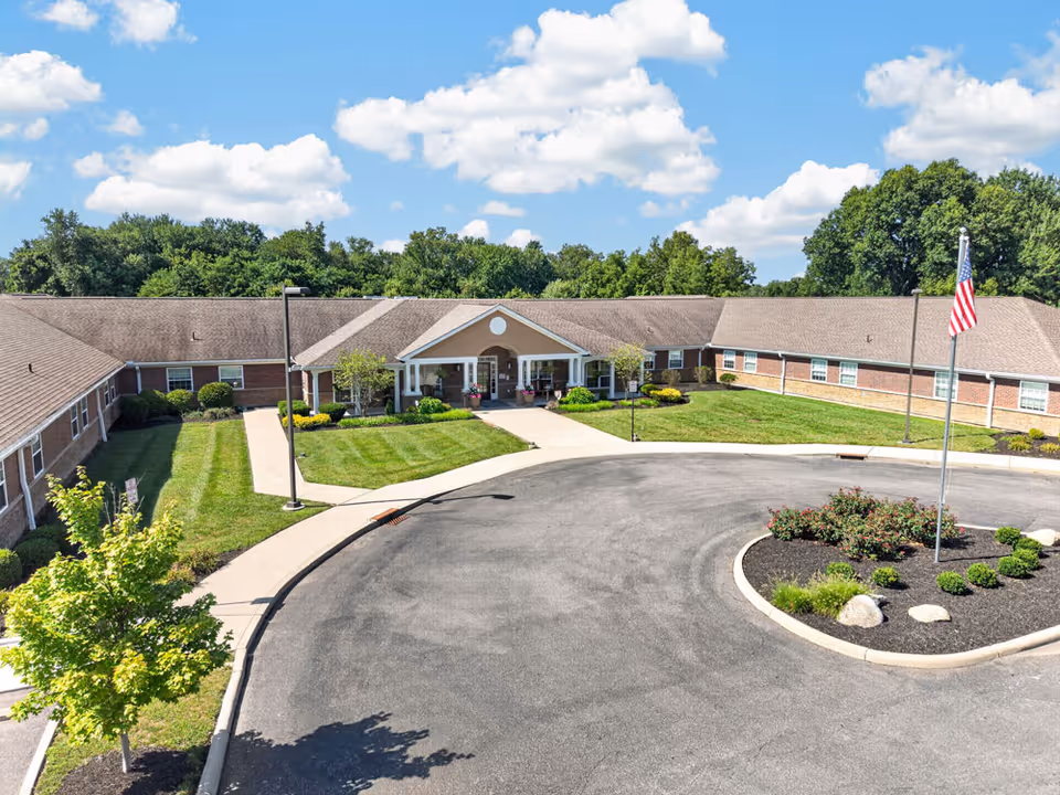 Single-story brick senior living facility front with circular driveway, landscaping, and American flag.