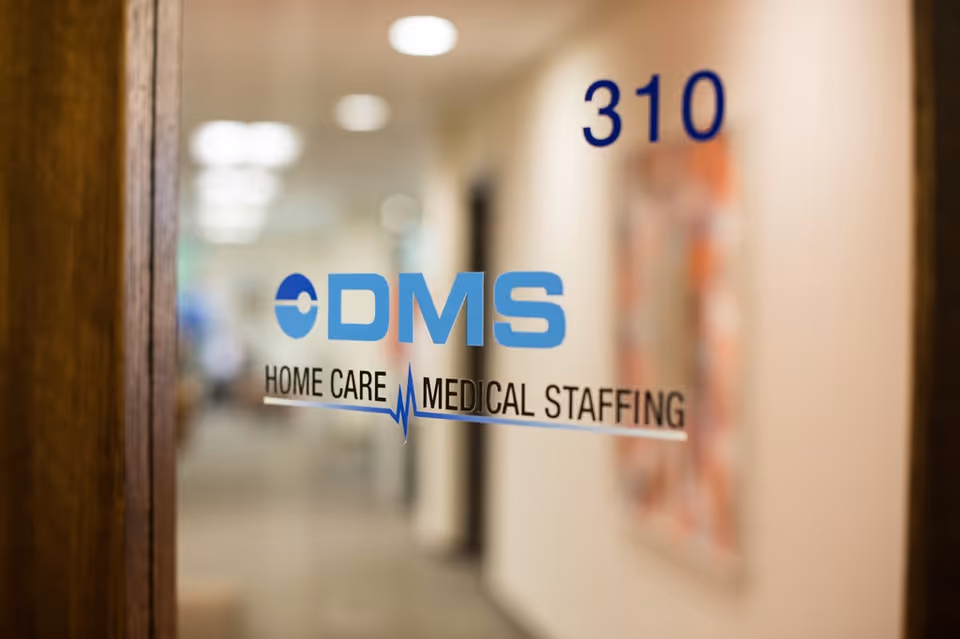Glass door with DMS Home Care Medical Staffing logo and 310, hallway blurred beyond