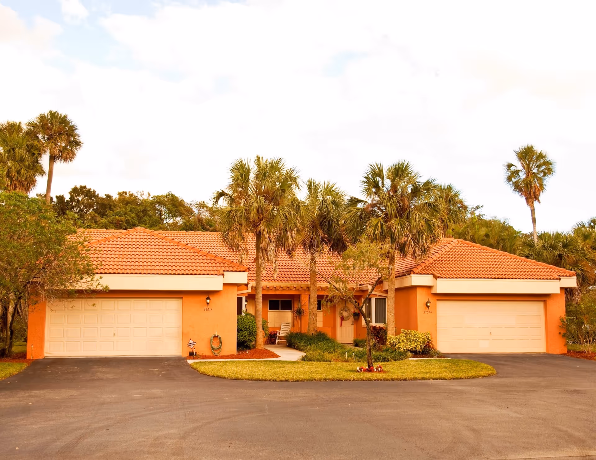 Two peach-colored residential buildings with tile roofs and palm trees along a circular driveway.