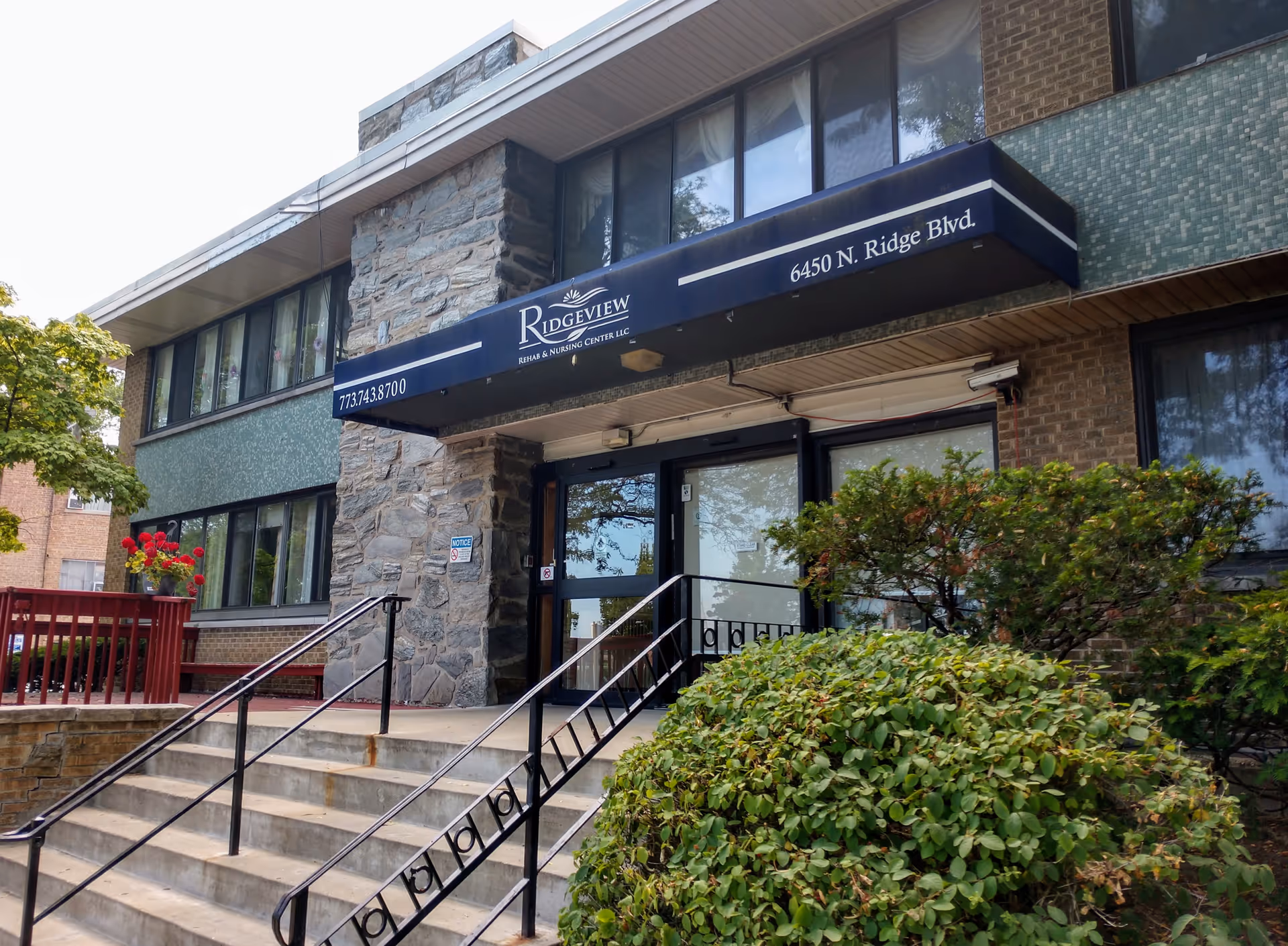 Exterior view of a senior living facility entrance with stairs and greenery.