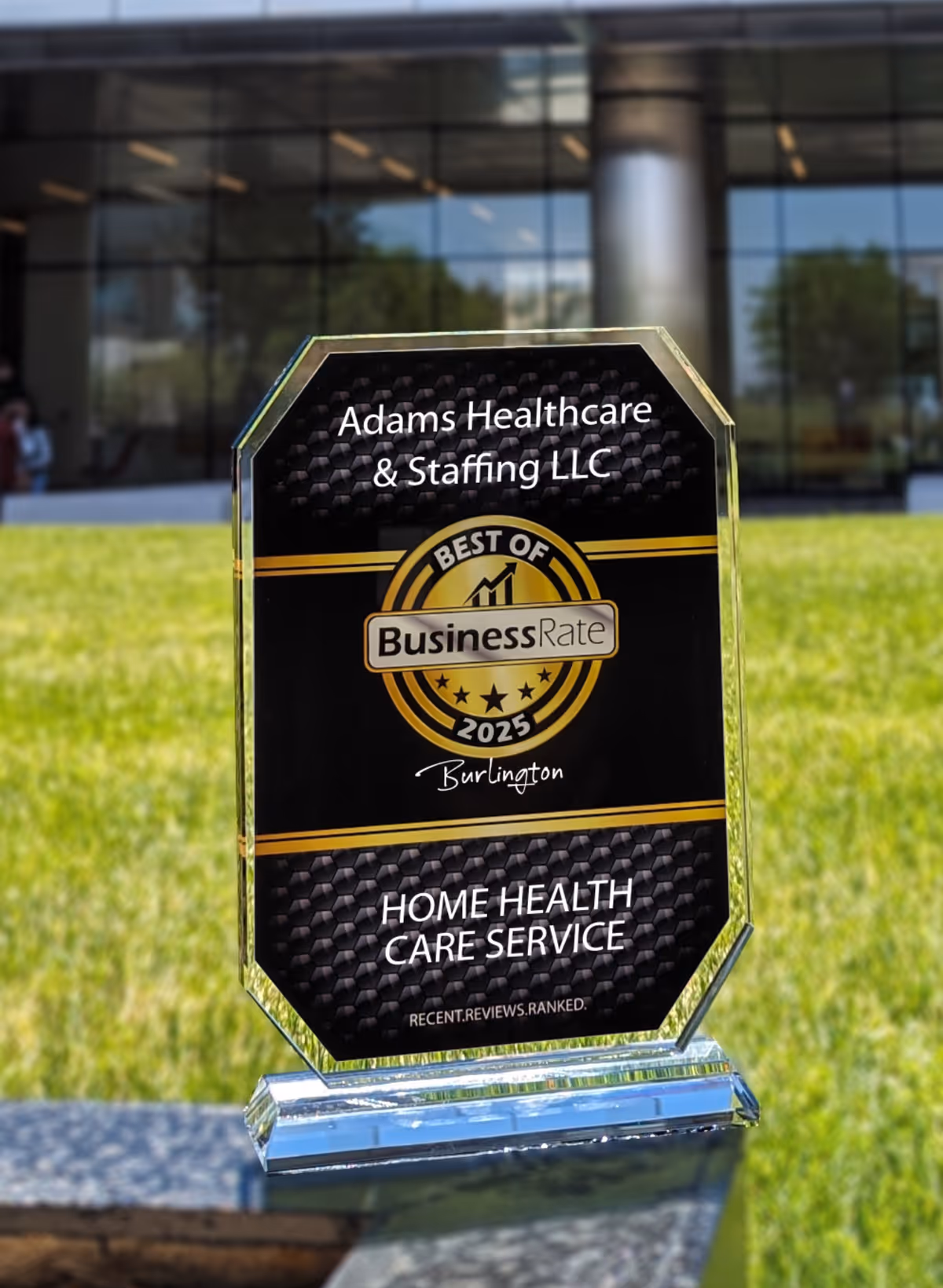 A glass award plaque sits on lawn in front of Adams Healthcare & Staffing LLC building.