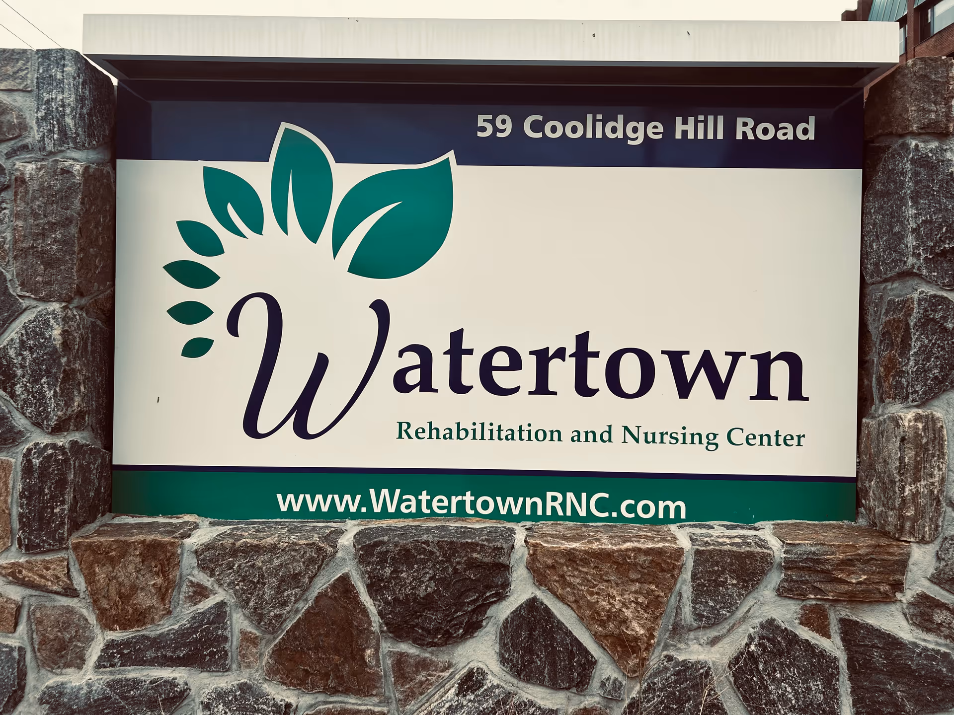 Sign for Watertown Rehabilitation and Nursing Center on a stone-faced wall.