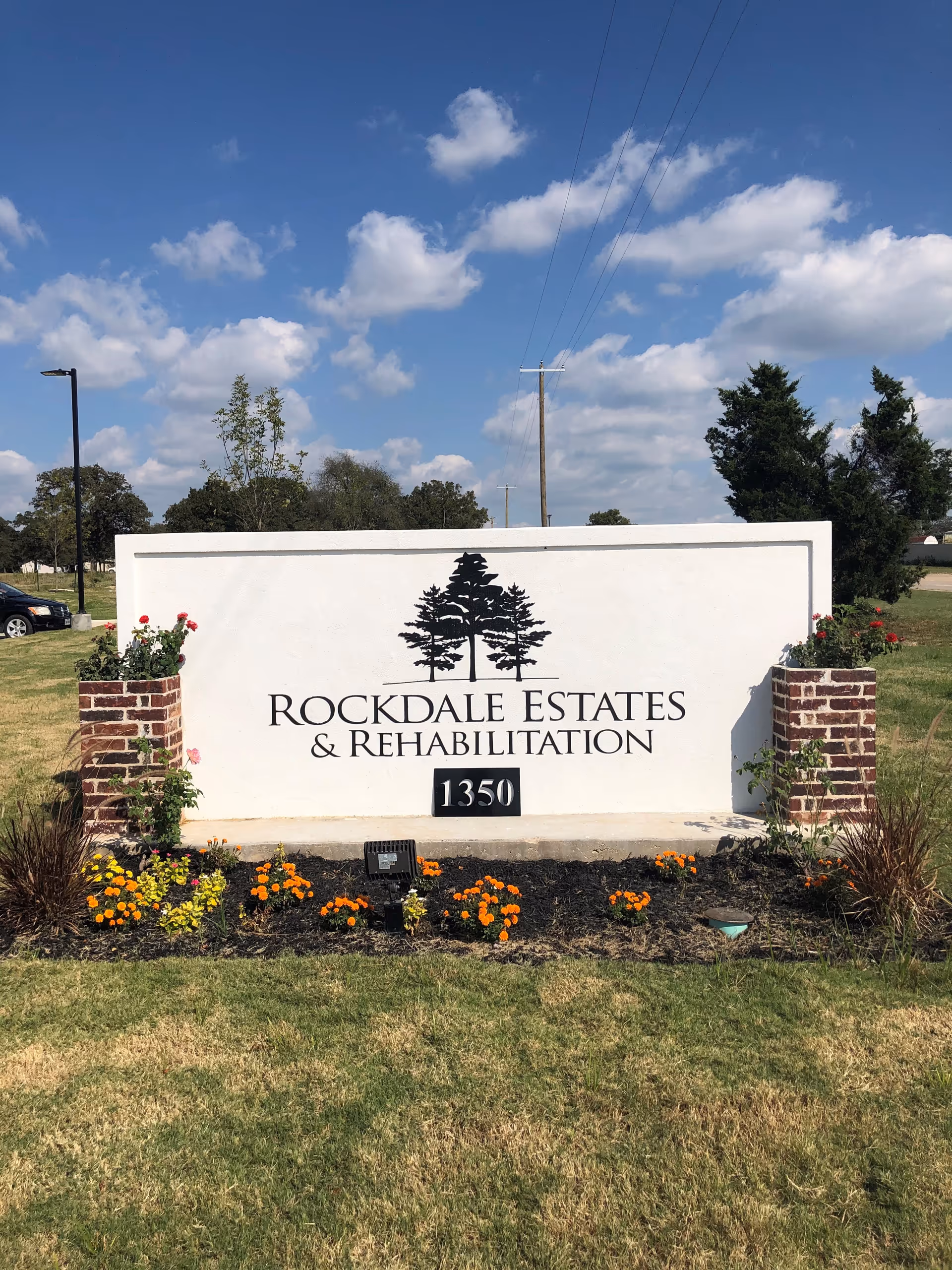 White stone sign reads Rockdale Estates & Rehabilitation with brick planters and flowers.