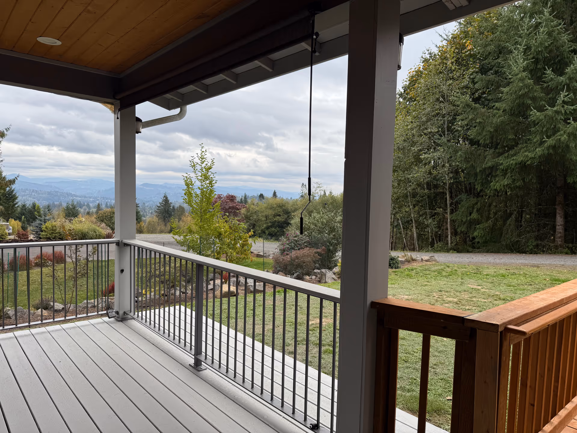 Covered wooden porch with railing overlooks a grassy yard and distant hills.